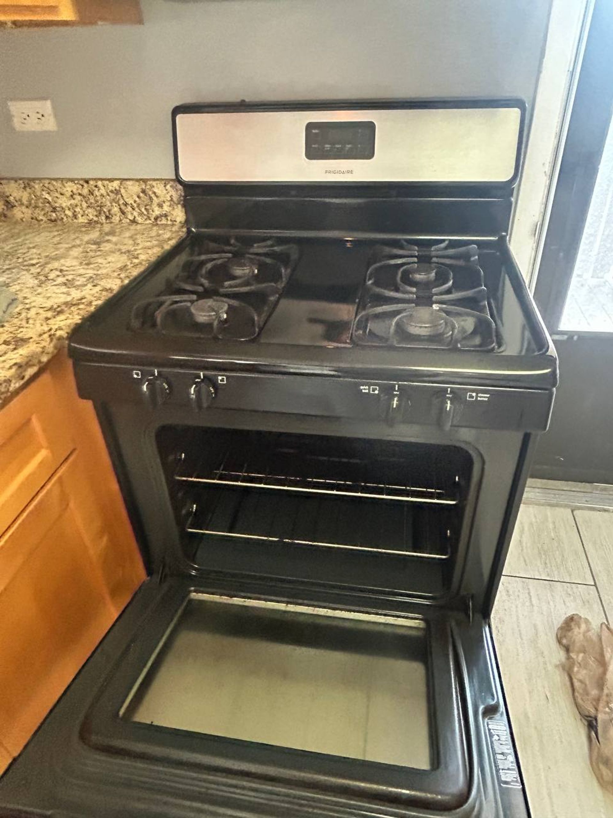 Open gas oven with clean racks beside granite counter