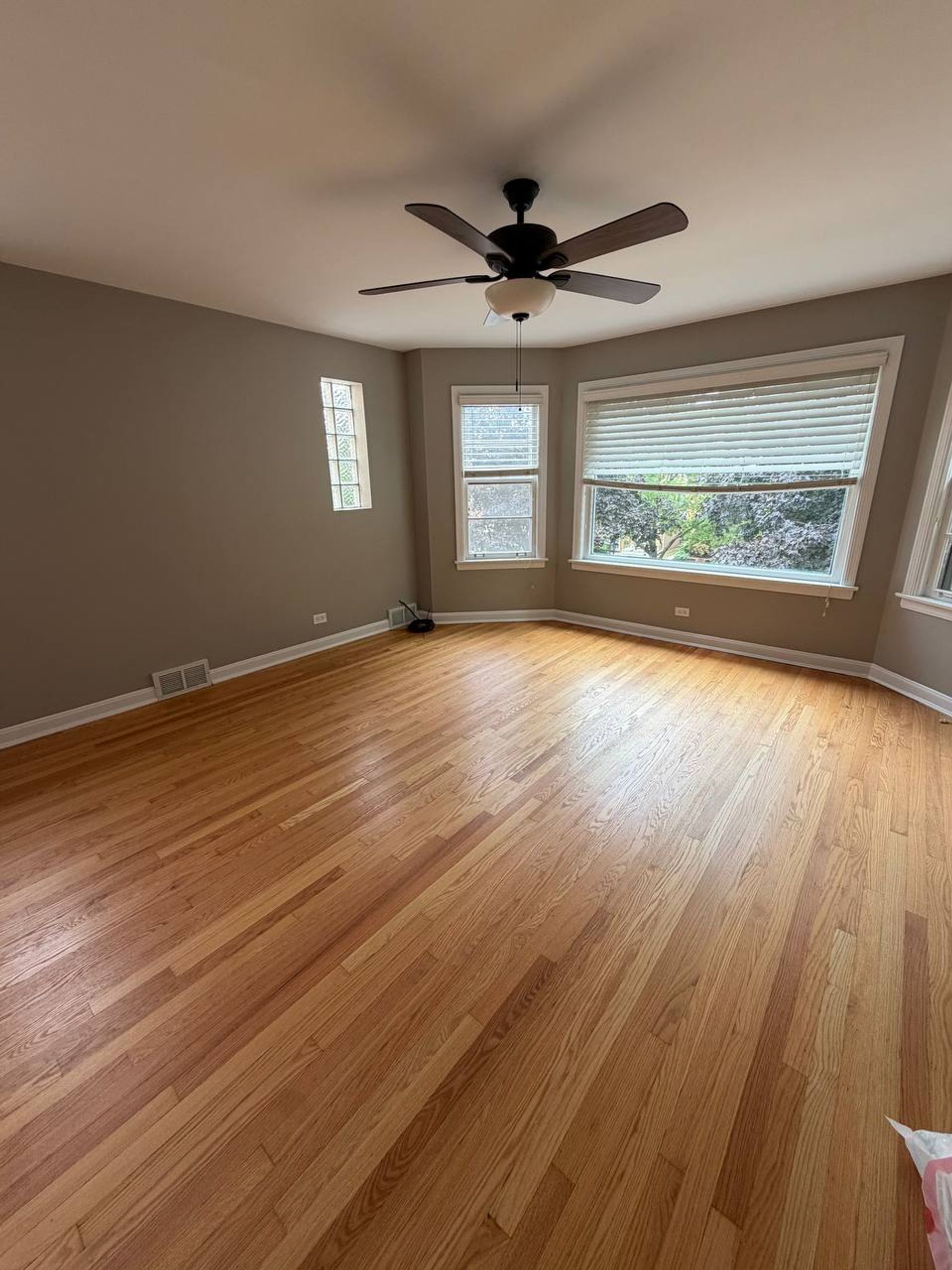 Empty living room with bay windows, ceiling fan and oak floor