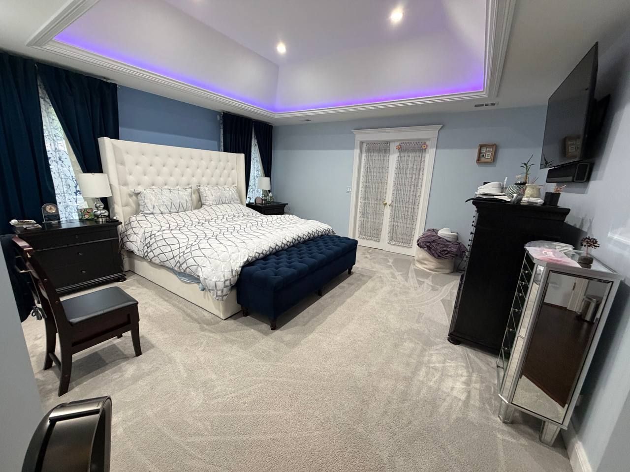 Large bedroom with tufted bed, navy bench and freshly vacuumed gray carpet