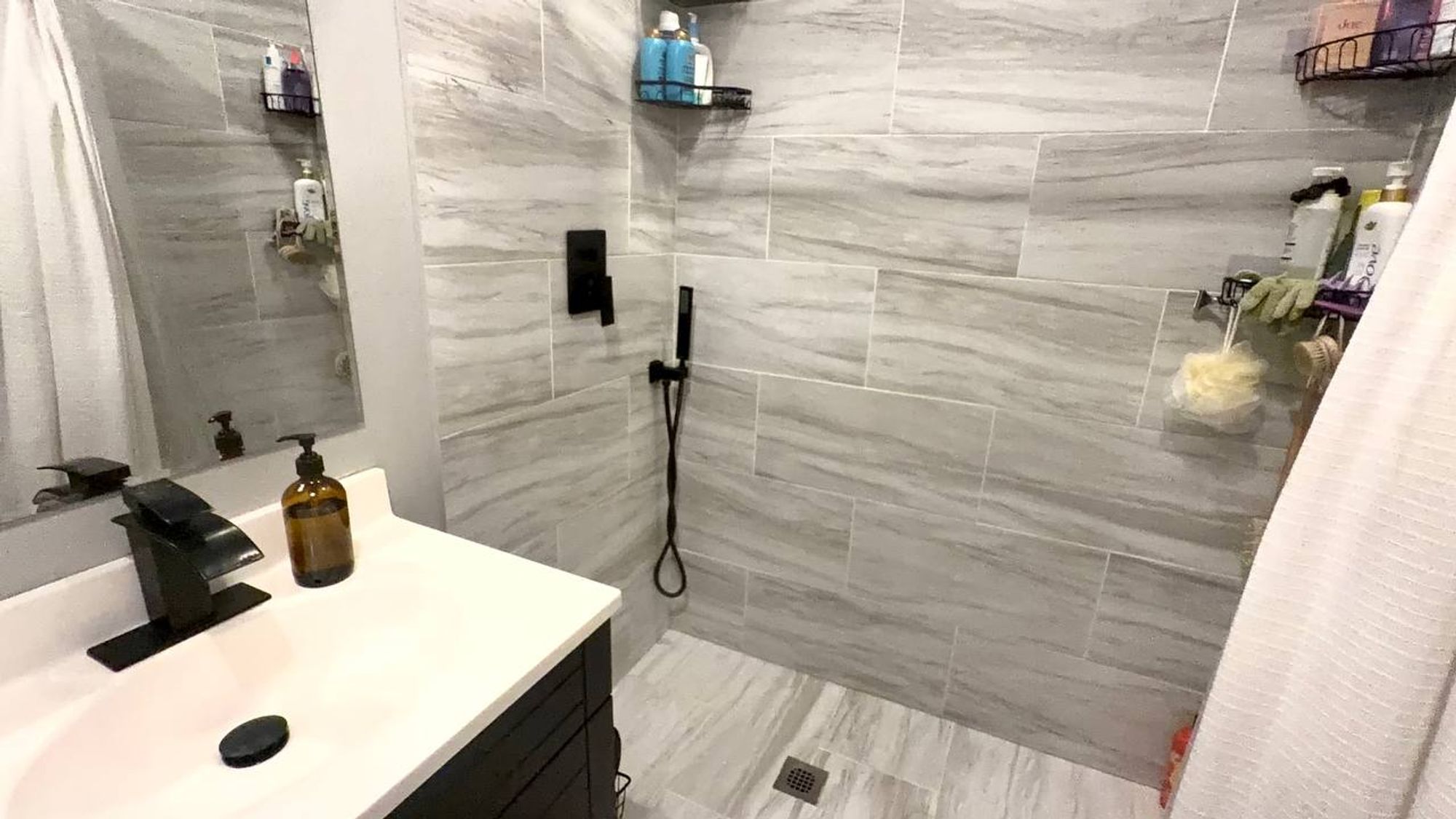 Curbless walk-in shower with gray tile and black hand shower