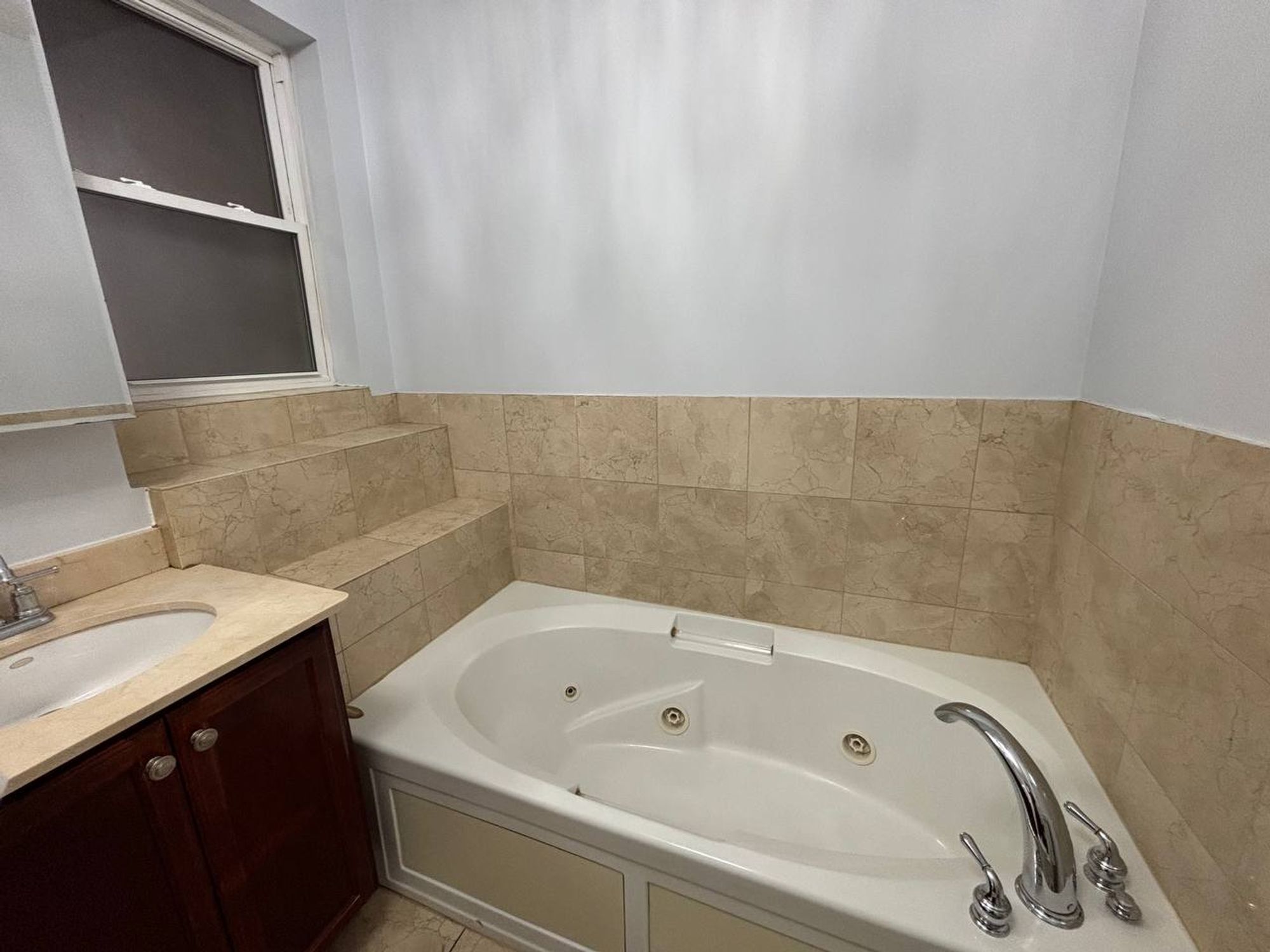 White jetted tub with chrome faucet and beige tile surround