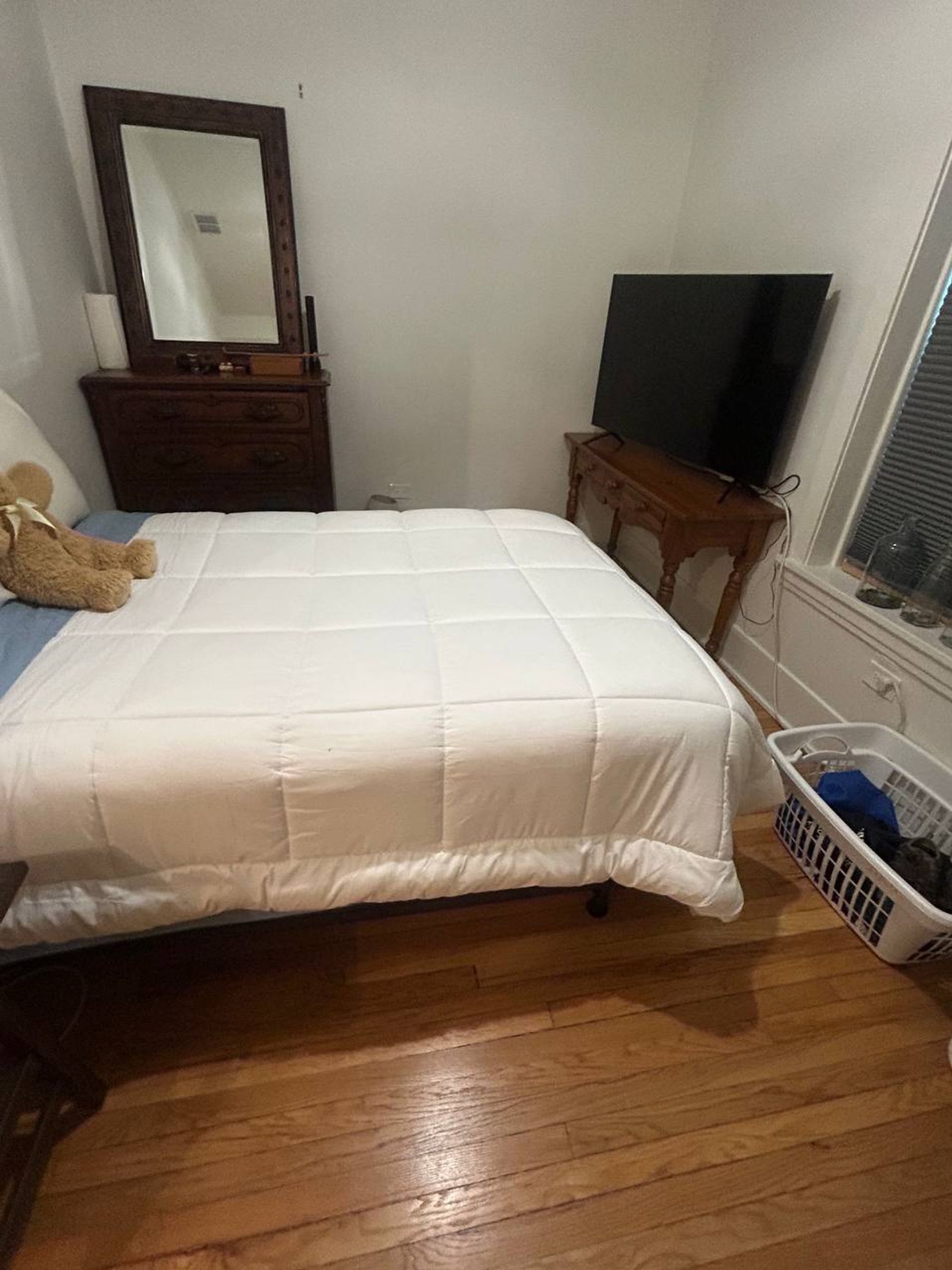 Bedroom with a made bed, wood dresser and hardwood floor