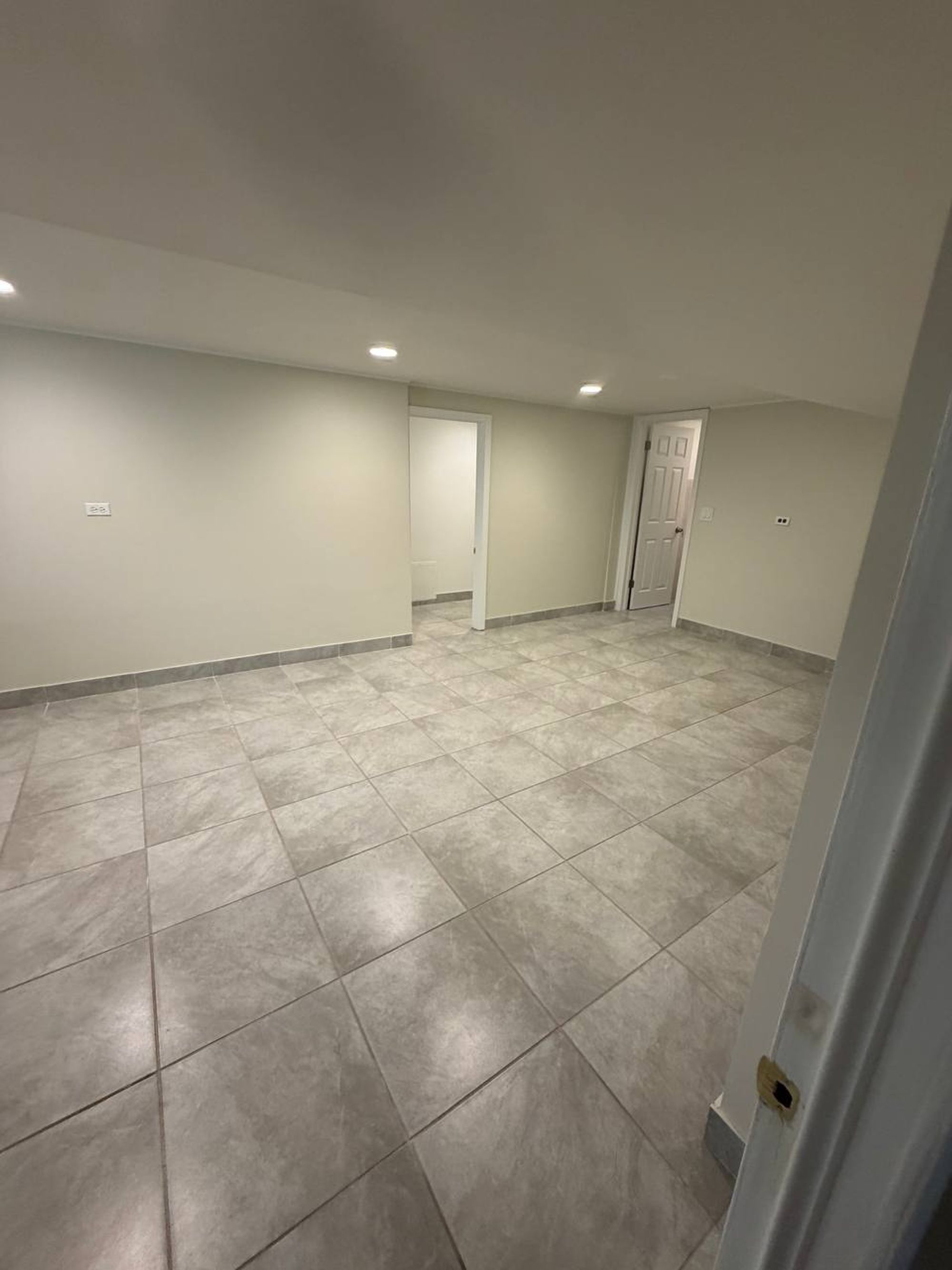 Empty finished basement room with large gray floor tiles