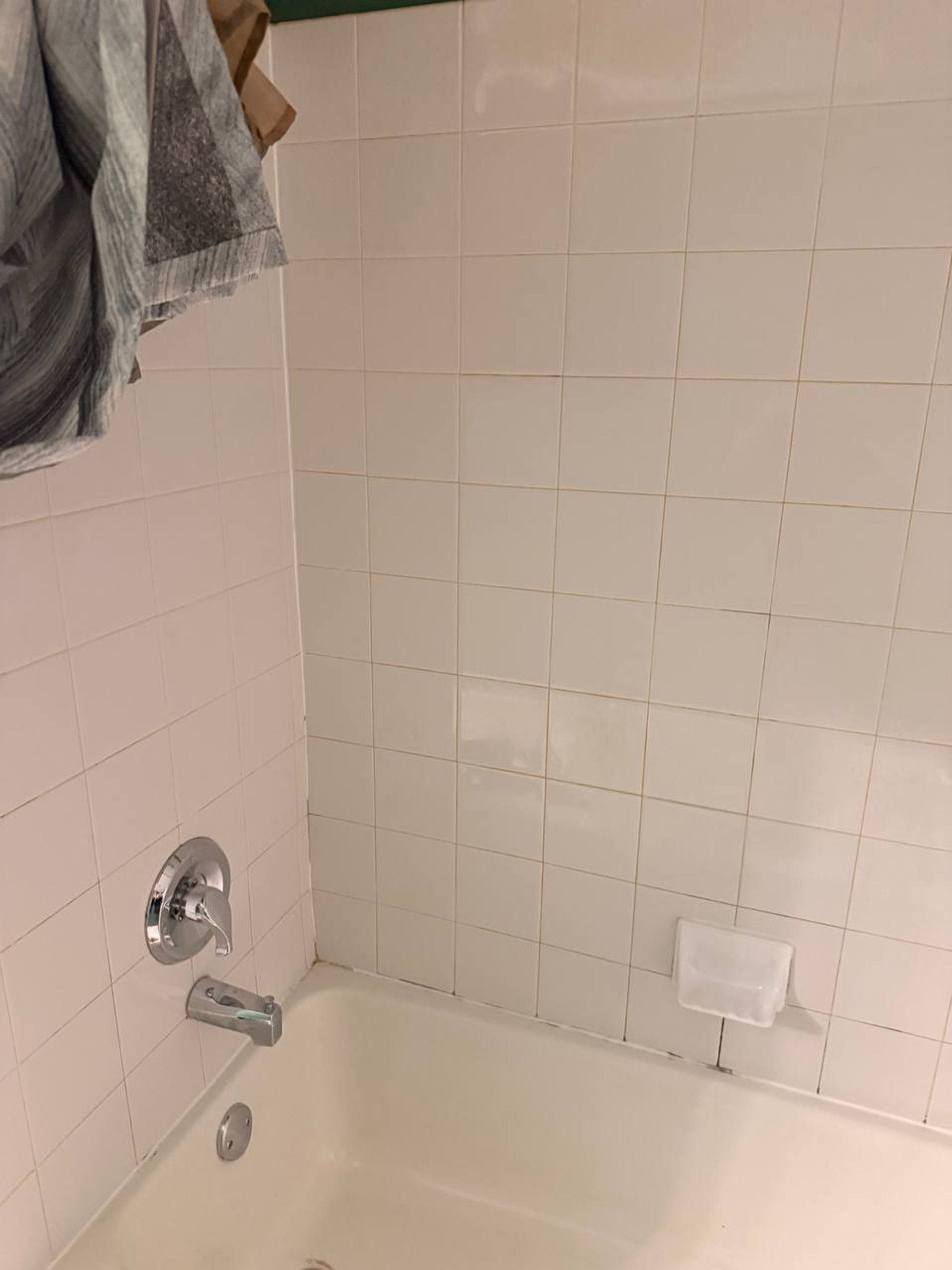 White tile tub wall with chrome handle and soap dish