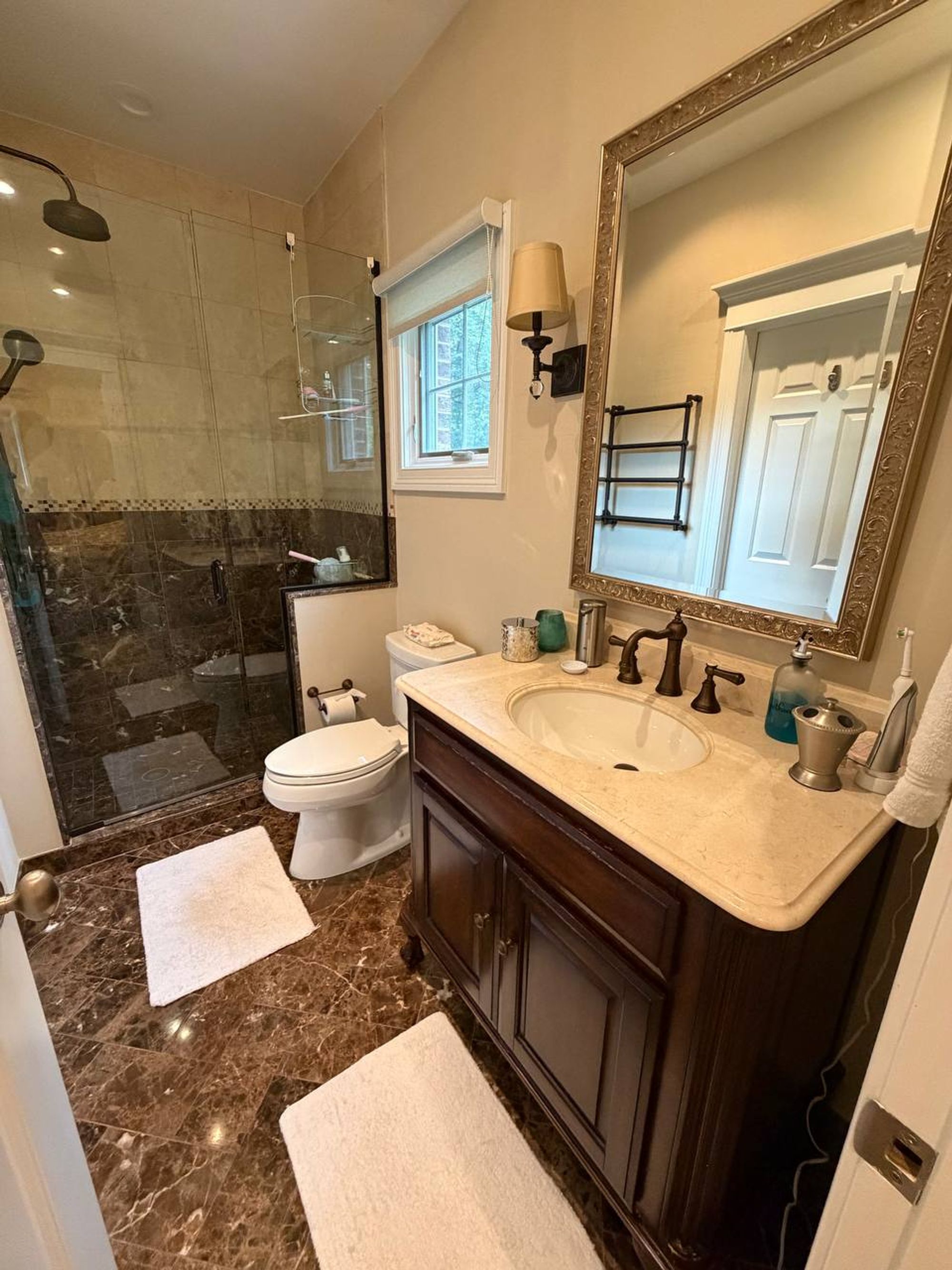 Bathroom with glass shower, brown marble floor and cream stone vanity