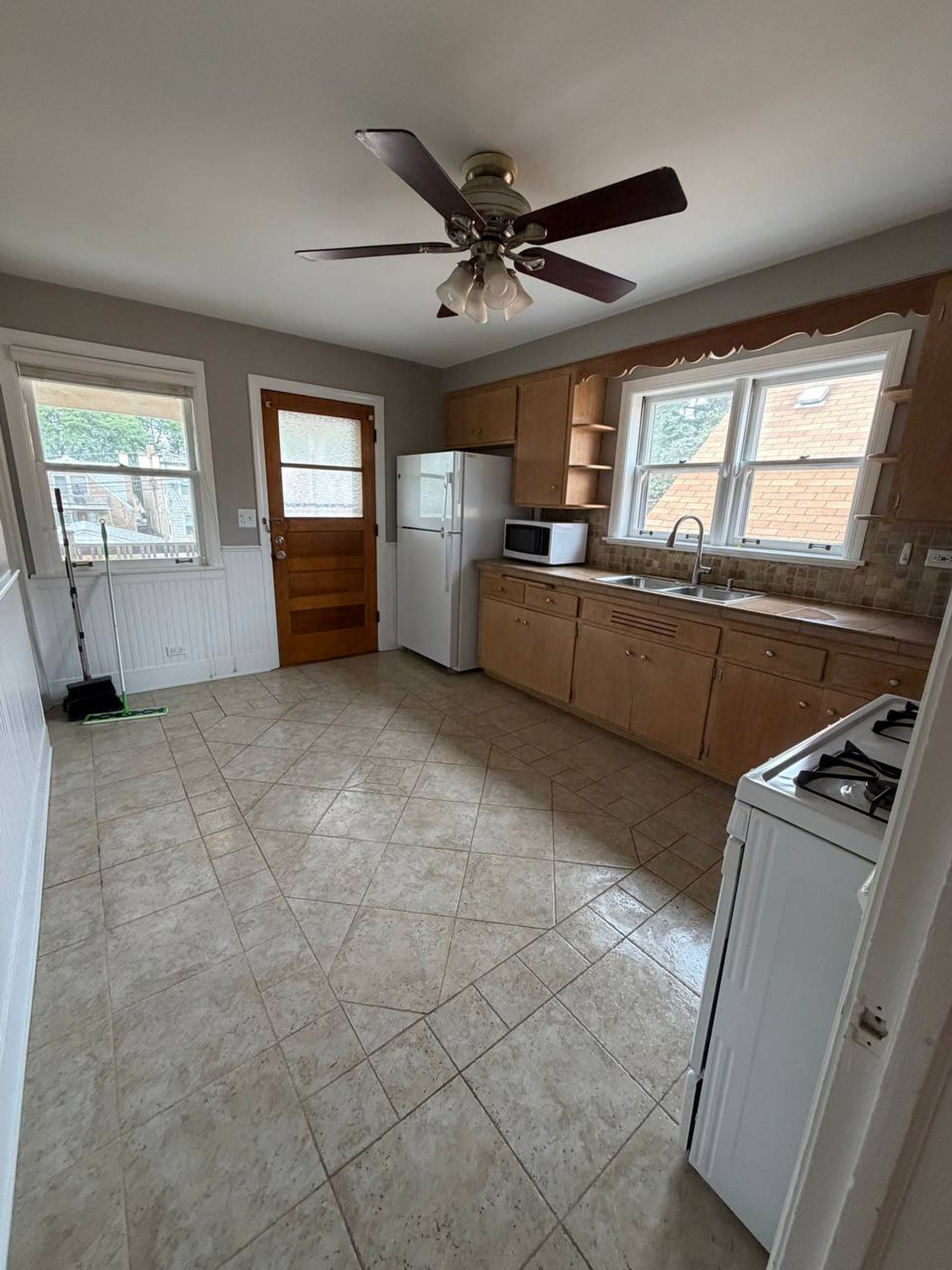 Empty kitchen with tile floor, white fridge, wood cabinets and gas range