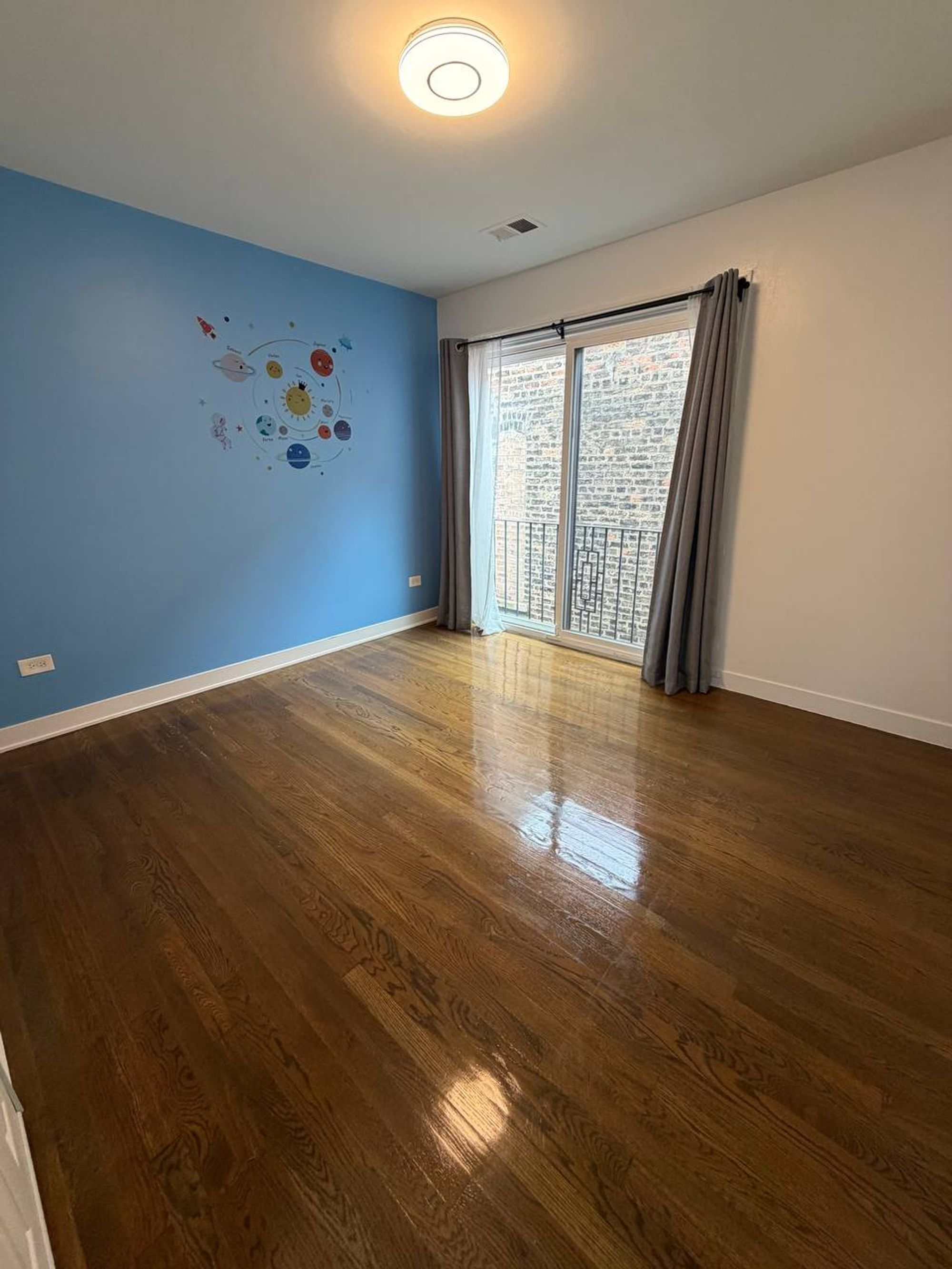 Empty bedroom with blue accent wall and shiny hardwood floor