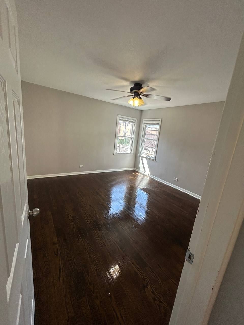 Empty corner bedroom with ceiling fan, two windows and dark floor