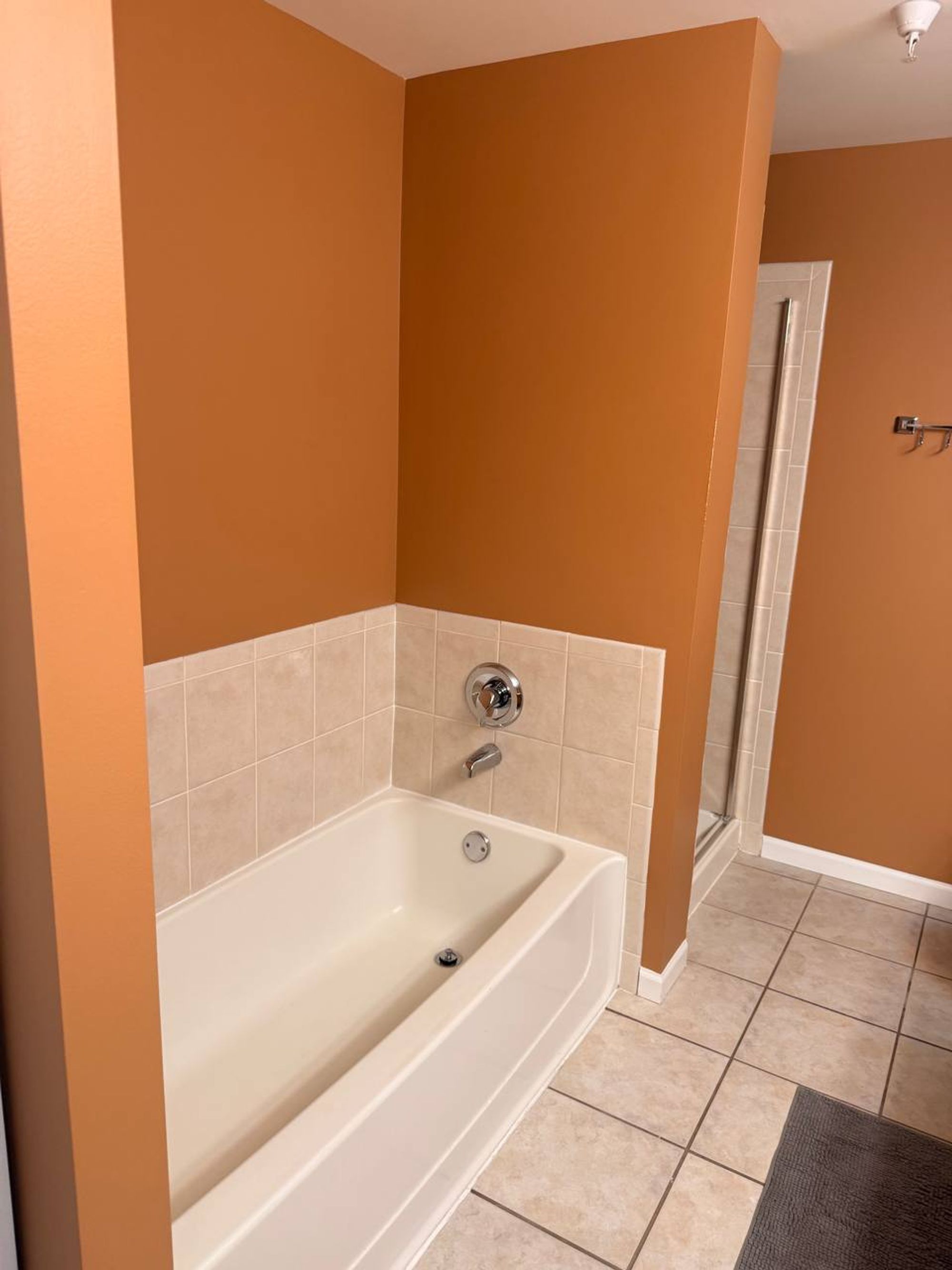 White soaking tub with beige tile surround and orange walls
