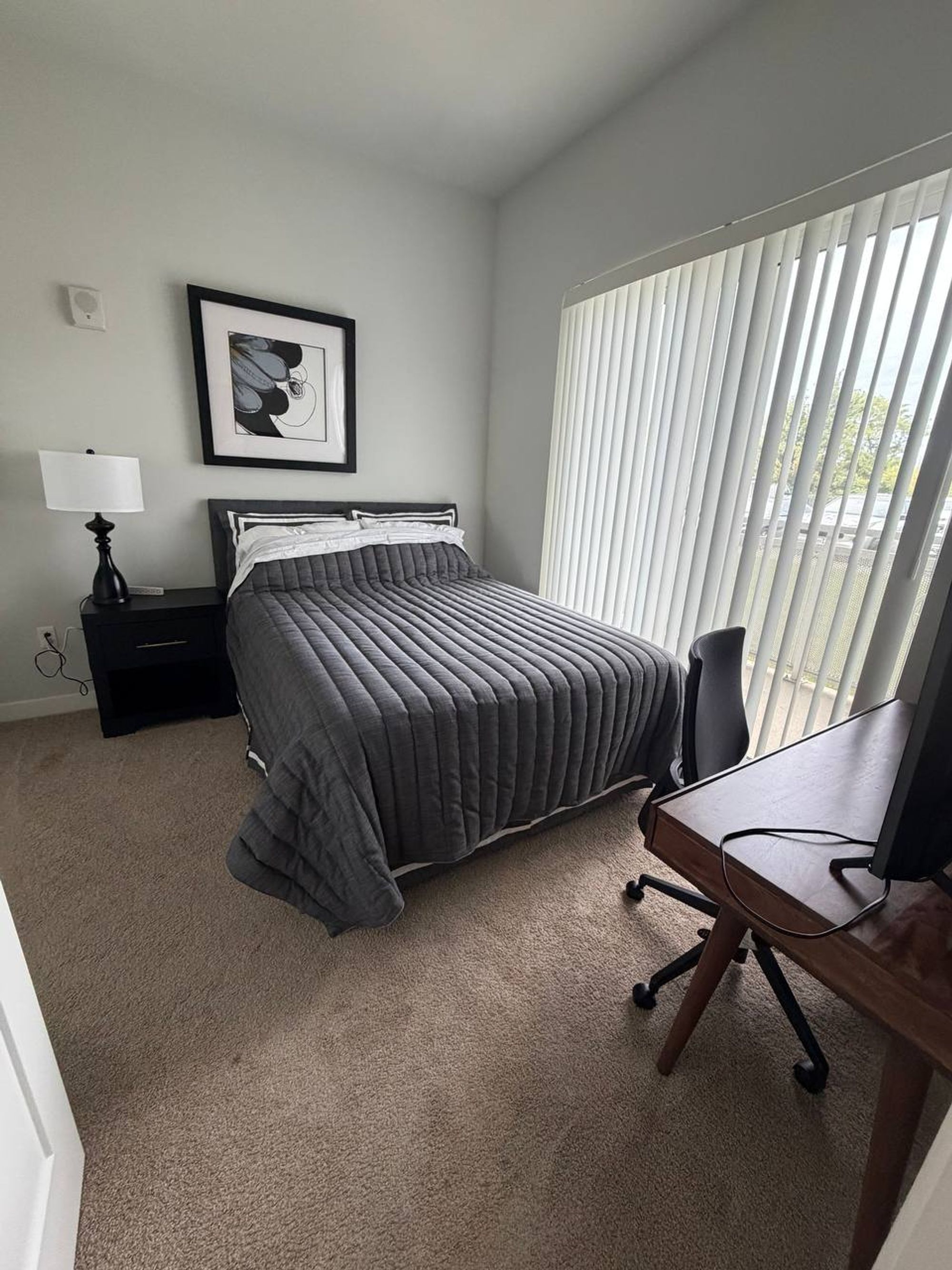 Guest bedroom with a made bed, framed art and a desk by the window