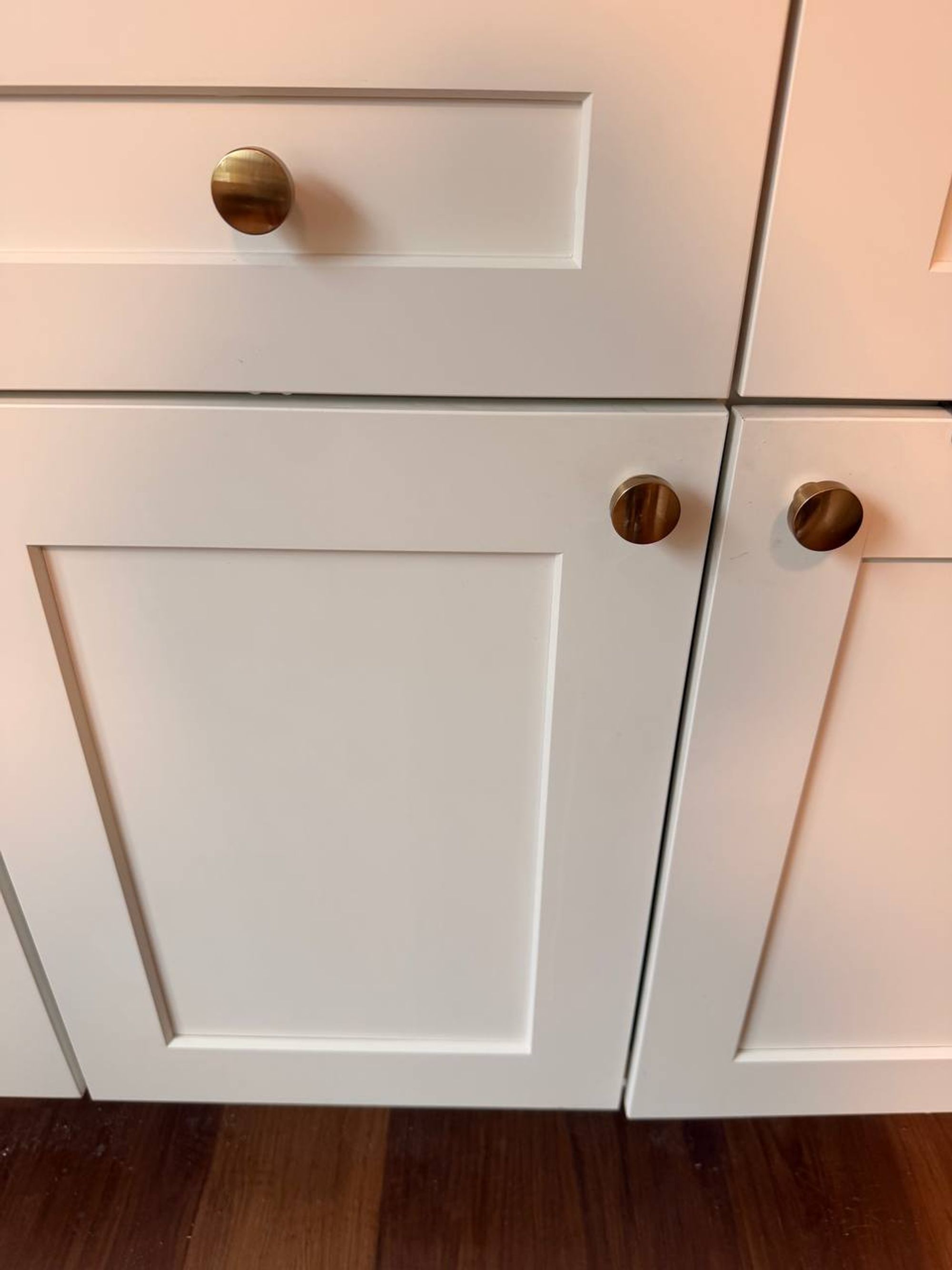 White shaker cabinet doors with brass knobs above a wood floor