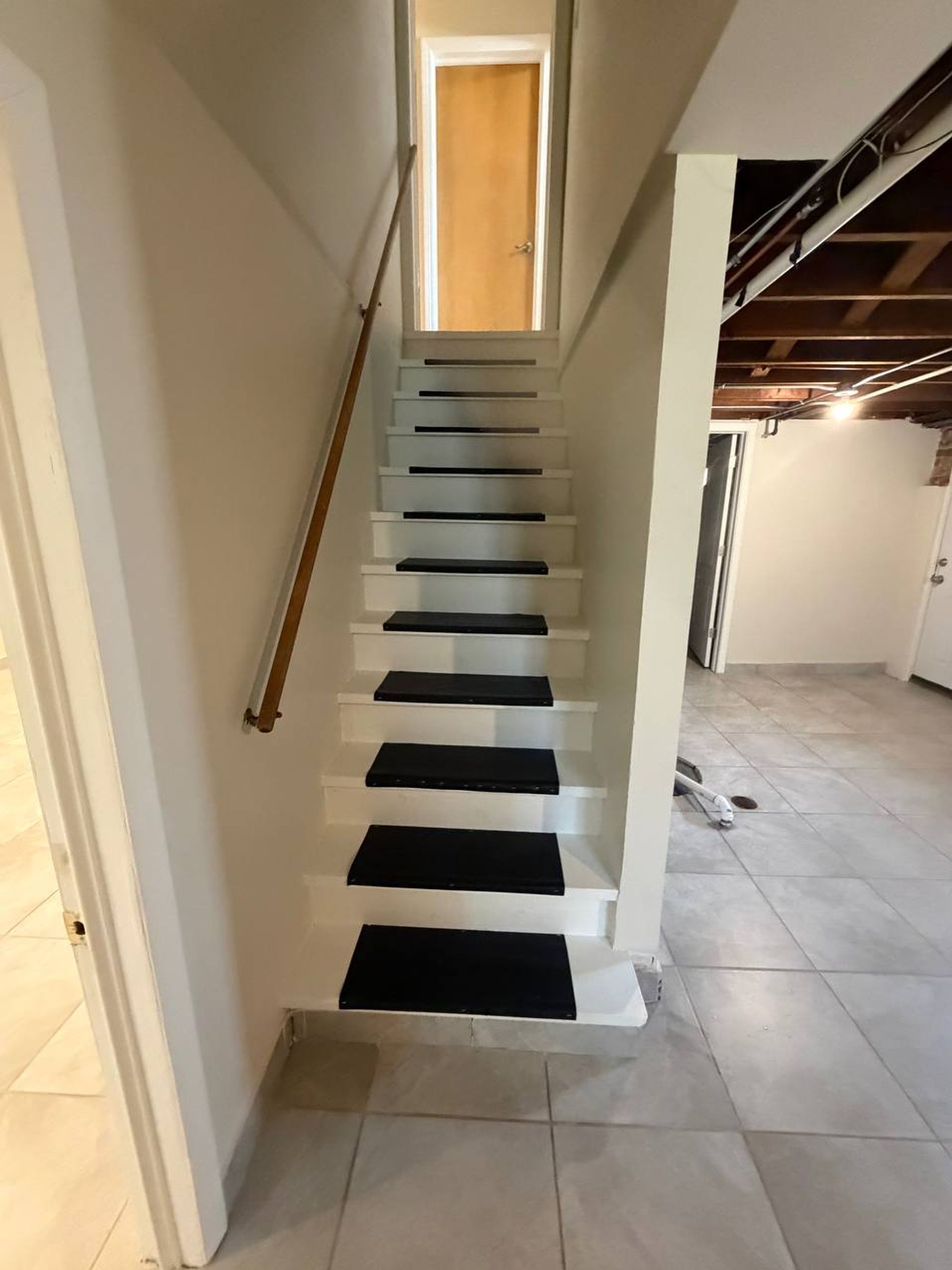Basement stairs with white risers, black treads and wood handrail