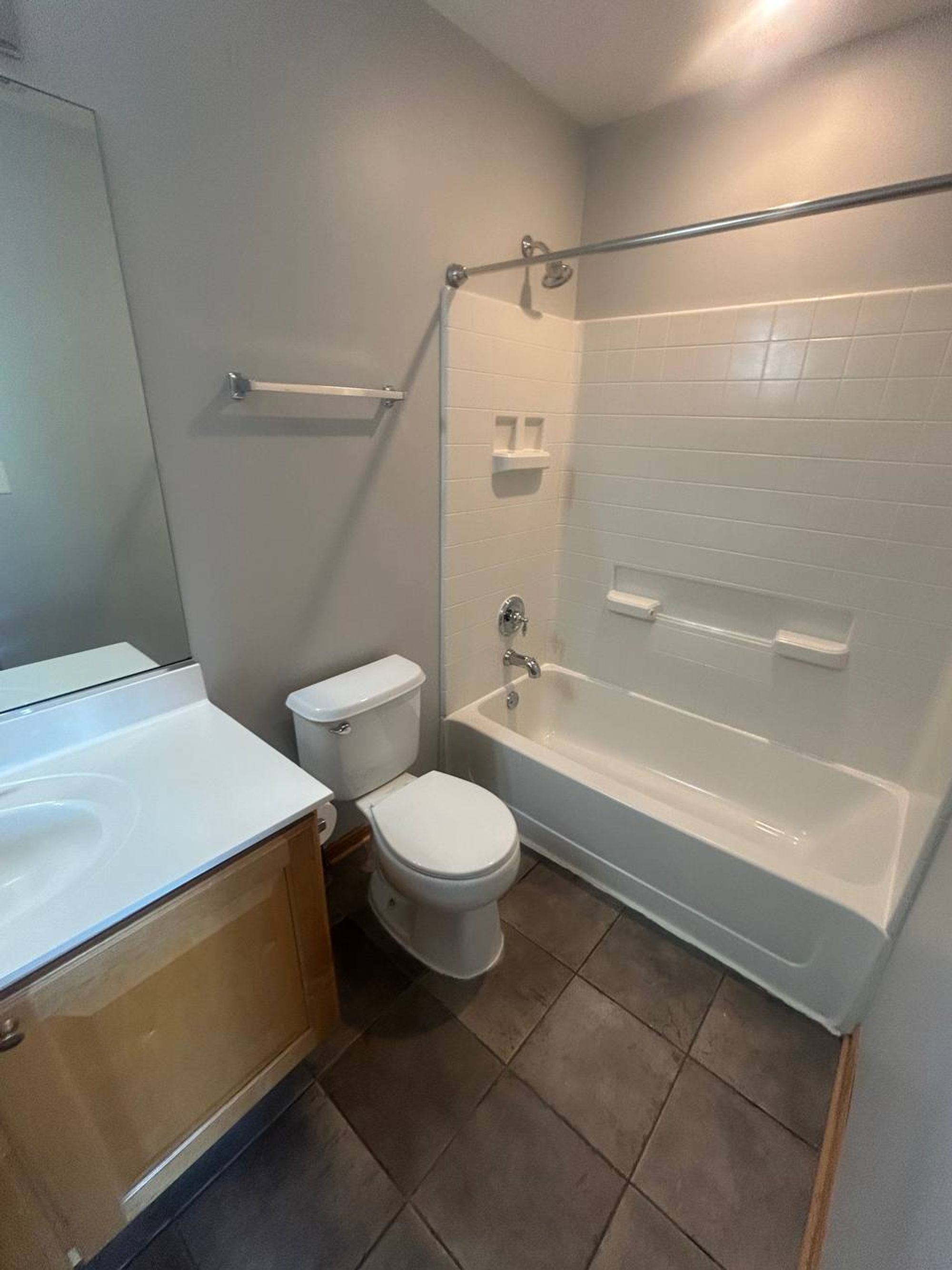 Bathroom with white tub surround, toilet and dark tile floor
