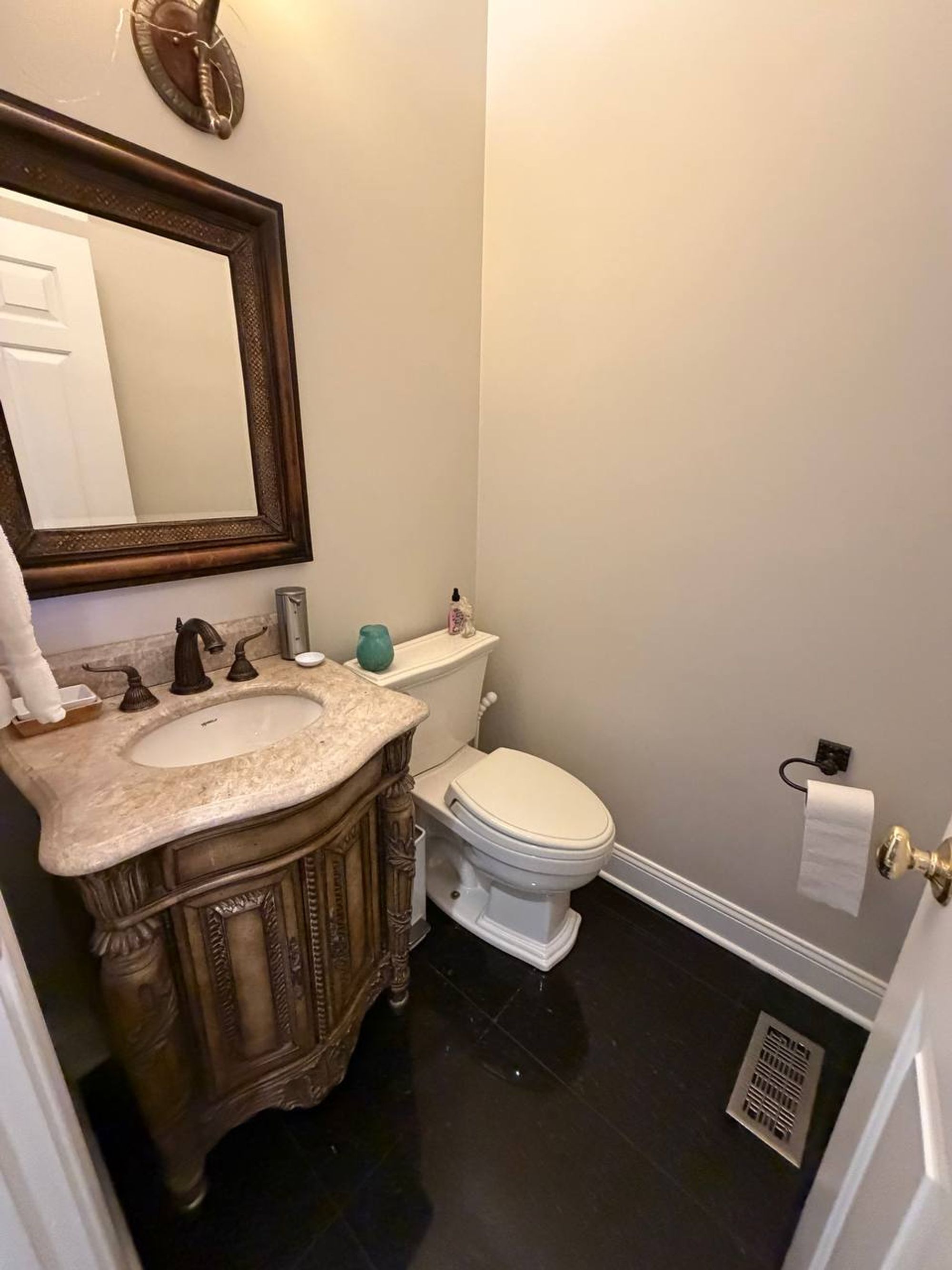 Powder room with carved wood vanity, stone counter and dark tile floor