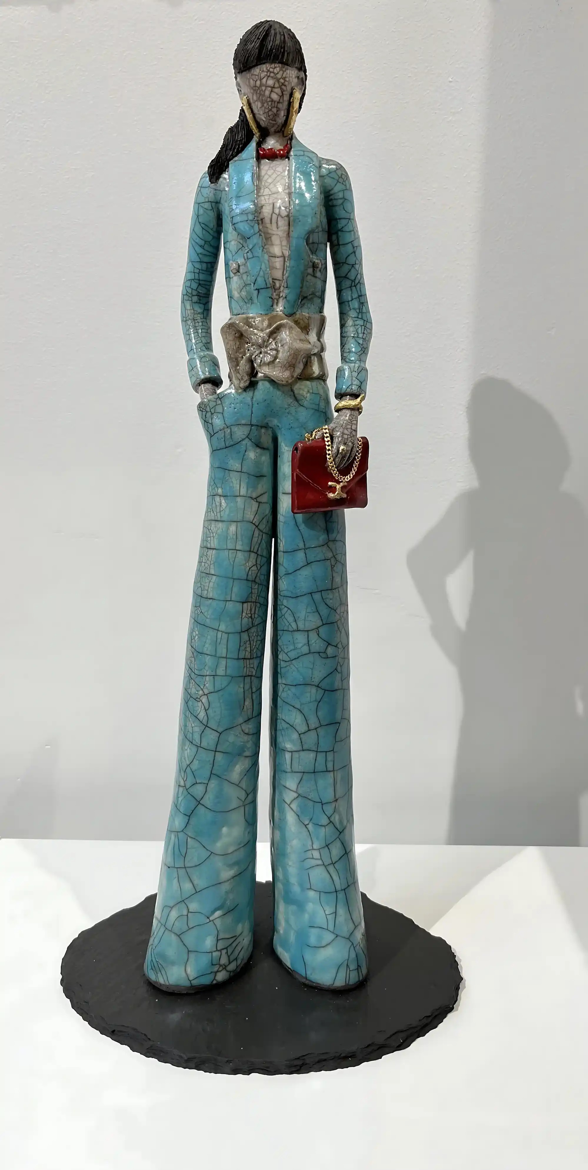 Sculpture Raku élégante en tenue de soirée : veste et pantalon turquoise craquelés, nœud papillon rouge, sac bordeaux à chaîne dorée