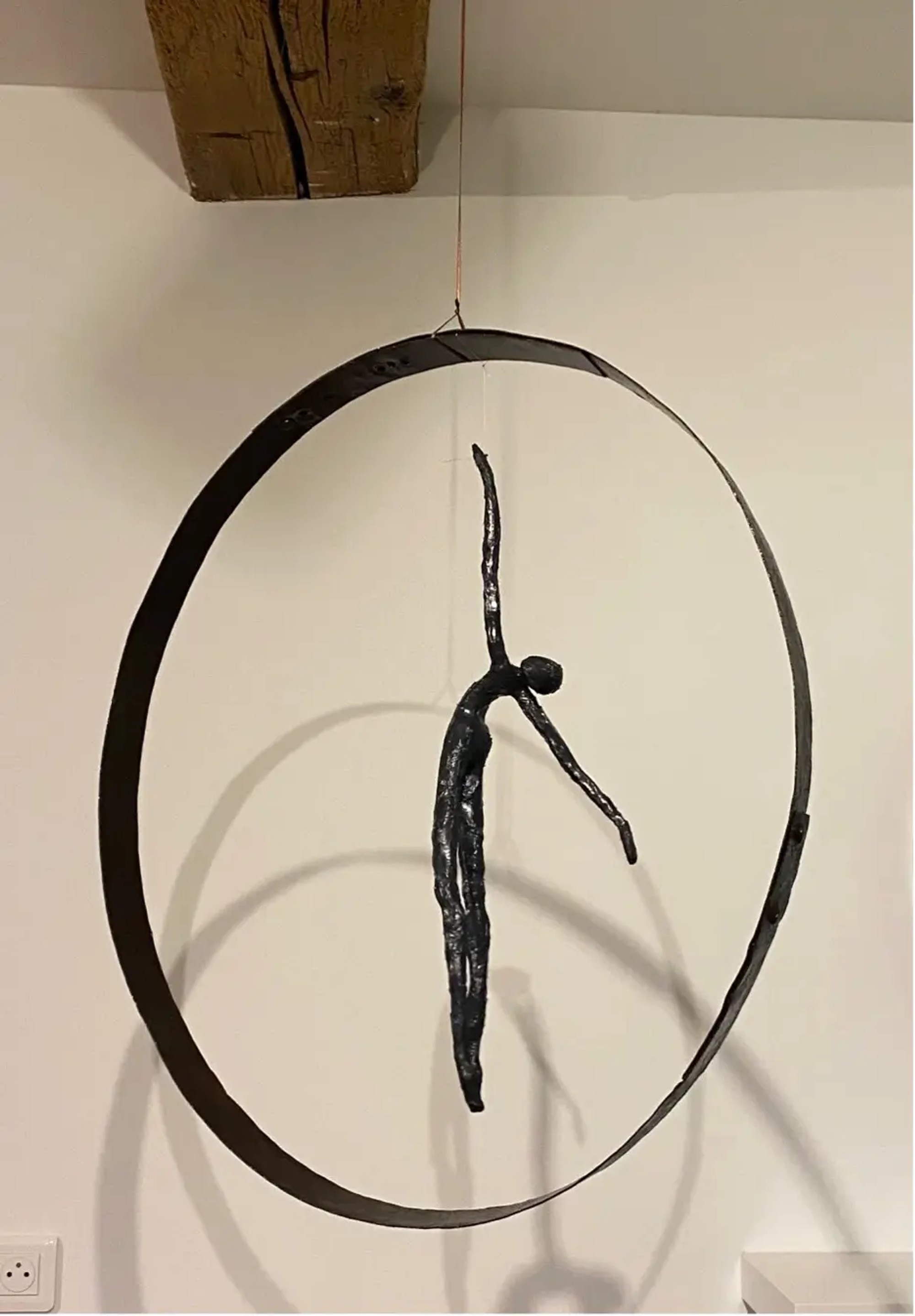 Sculpture en métal d'une silhouette élancée en extension à l'intérieur d'un cercle suspendu, incarnant l'élan et la tension