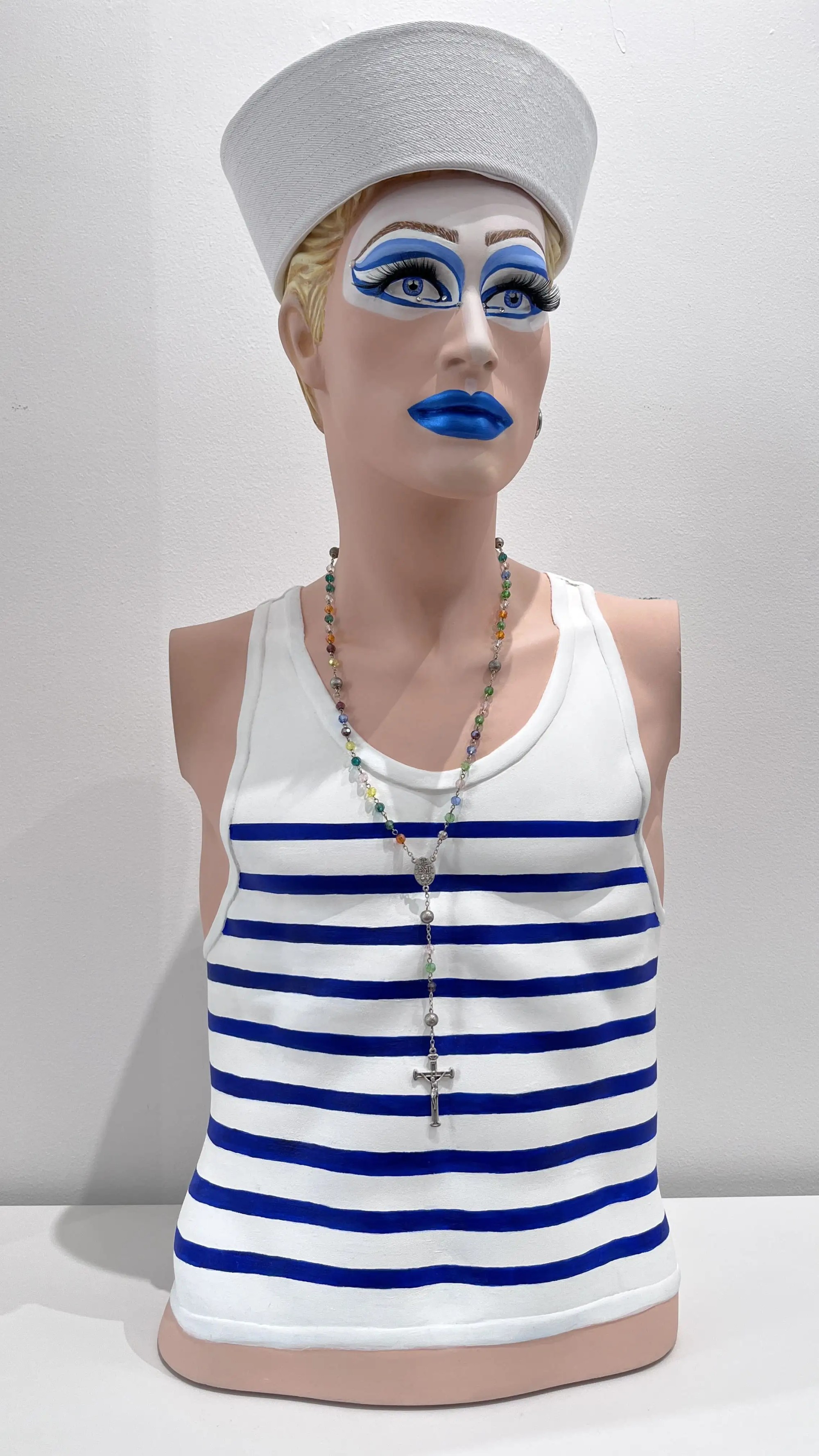 Buste de matelot au maquillage bleu graphique, marinière blanche et bleue, chapelet coloré, style pop art.