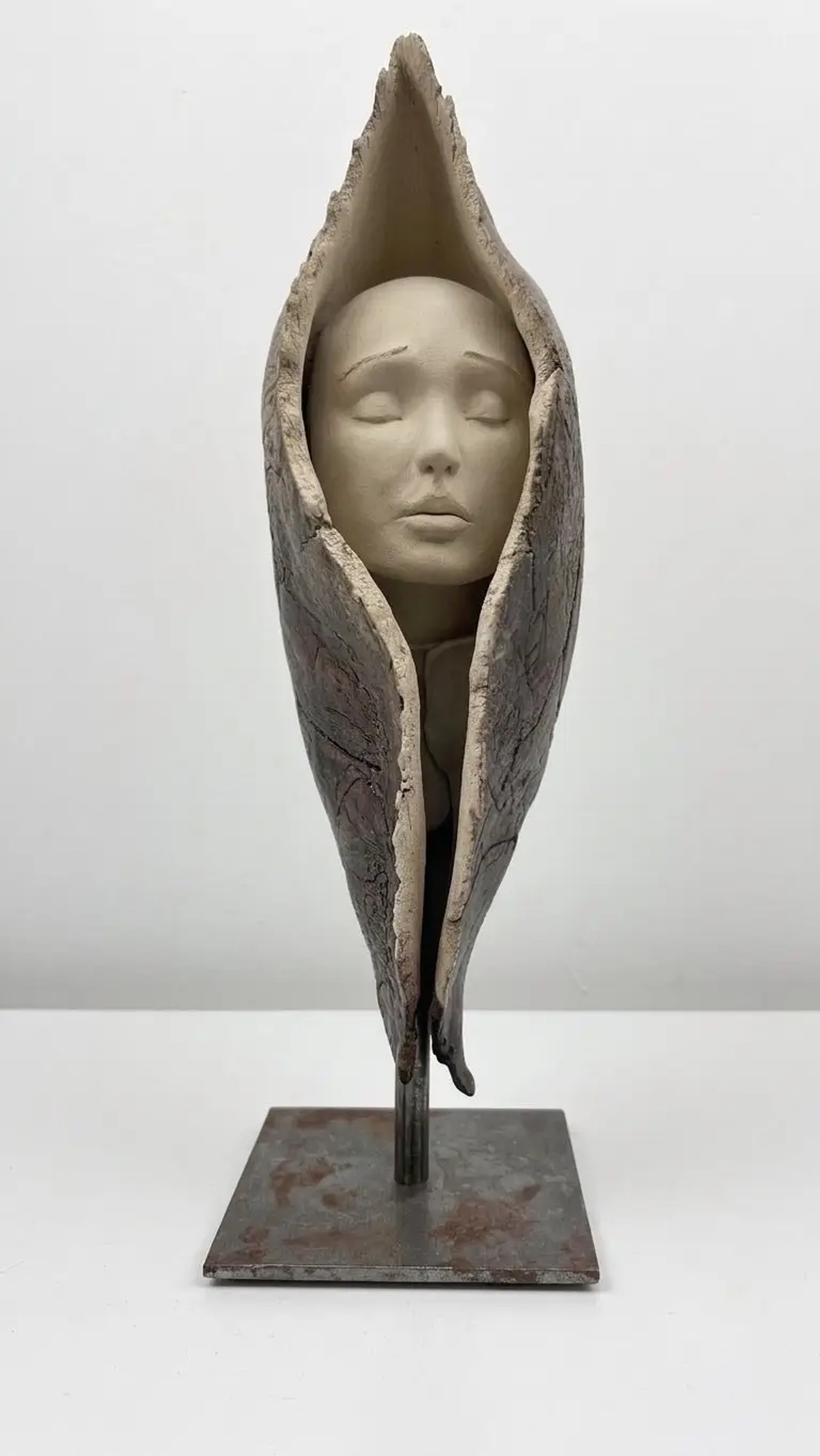 Sculpture en grès beige et gris sombre représentant un visage serein enveloppé dans une forme organique protectrice verticale.