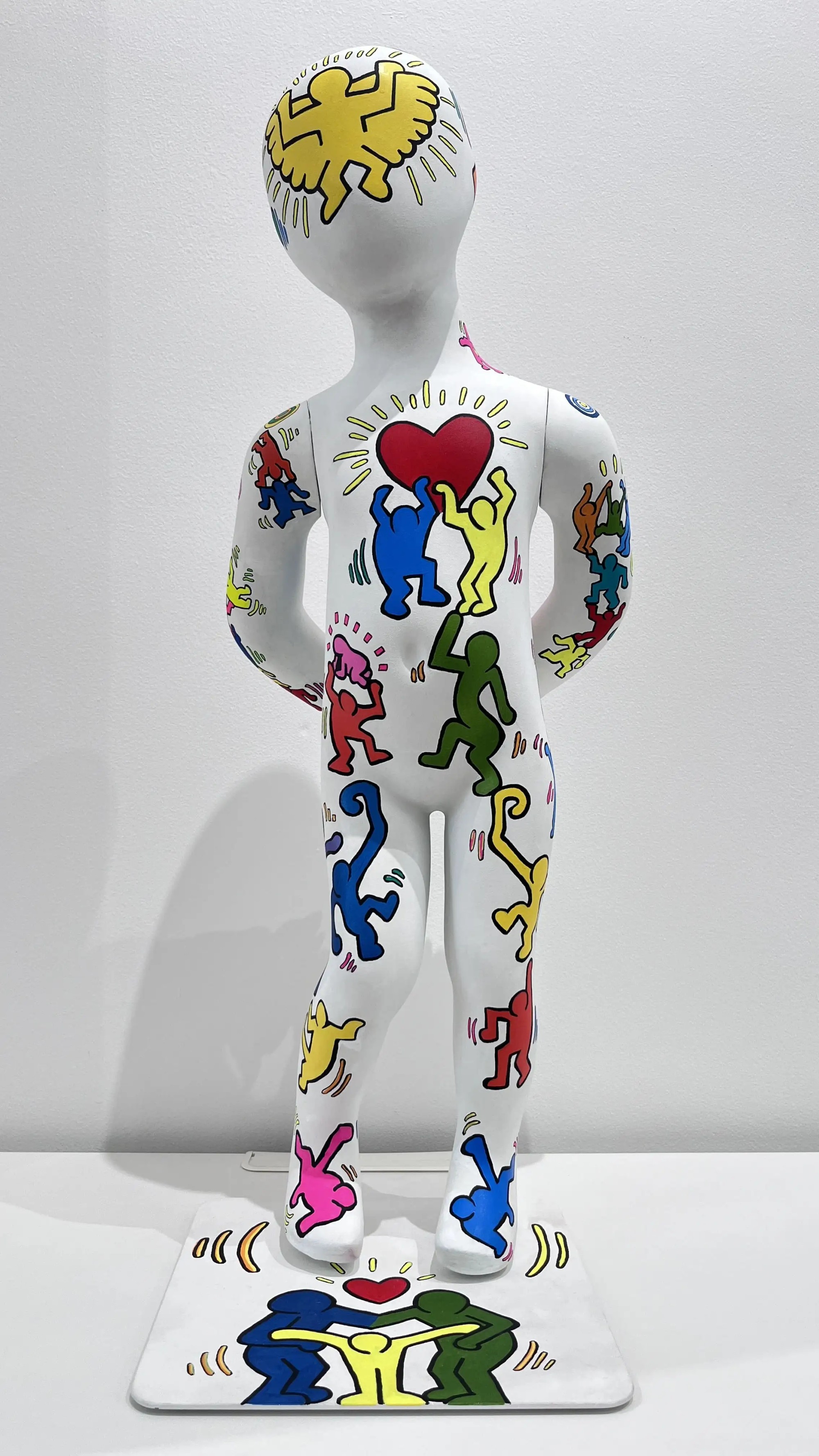 Sculpture enfant blanc peint de figurines colorées façon pop art, cœur rouge central, corps dynamique.