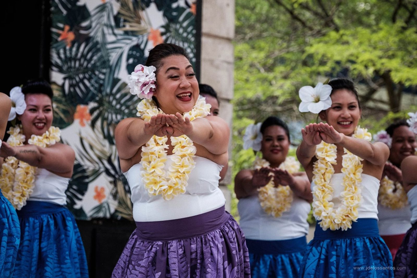 A joyful group of hālau dancers extending their hands toward the audience