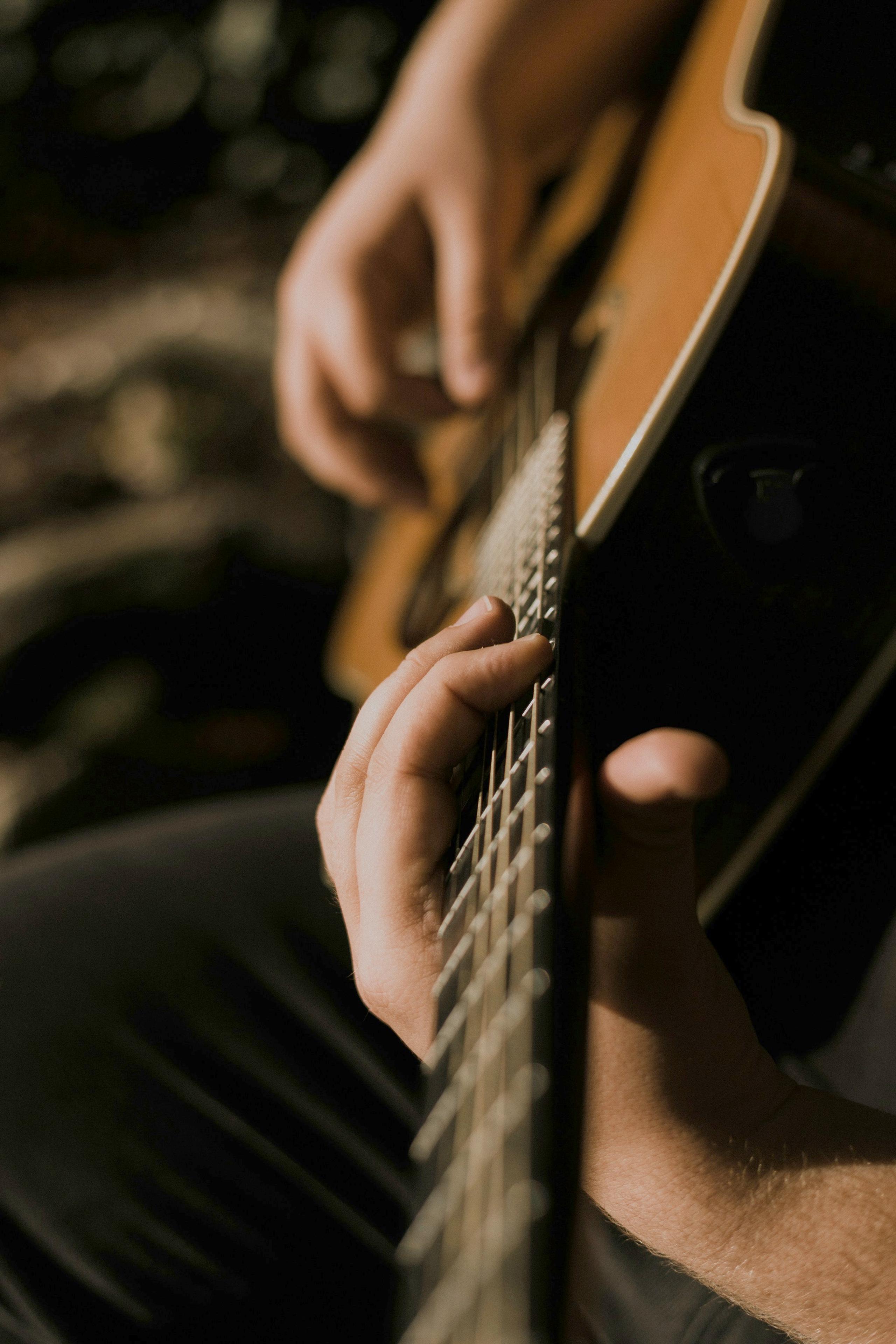 Hands playing an acoustic guitar in low light