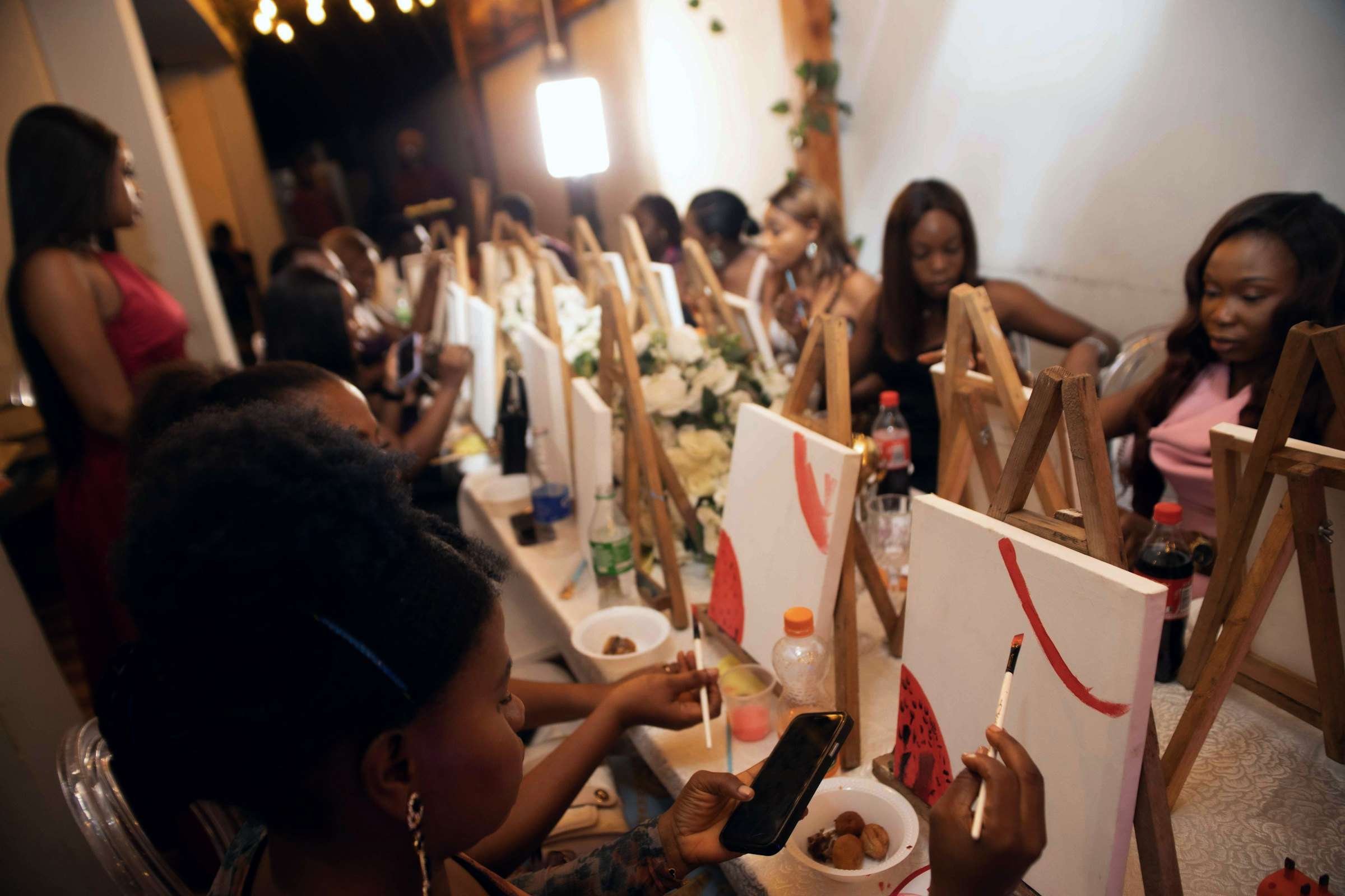Canvases on easels down a long table at a paint-and-sip evening