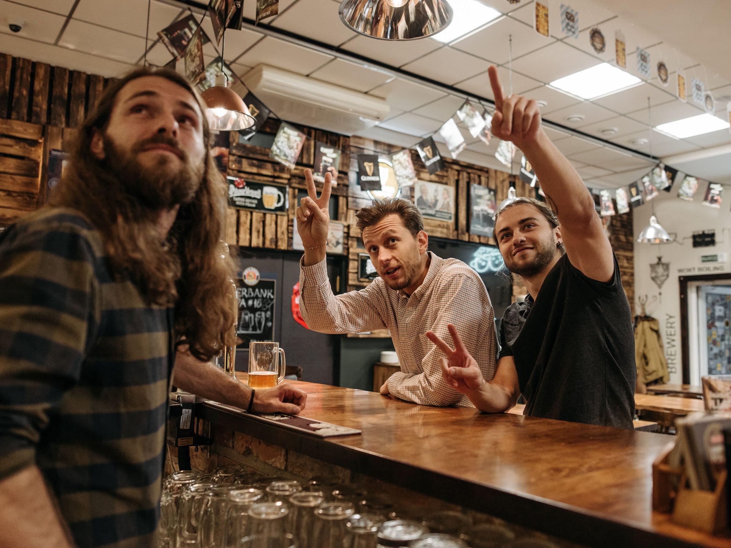 Illustrative photograph of friends at a wooden bar, one pointing up with the answer