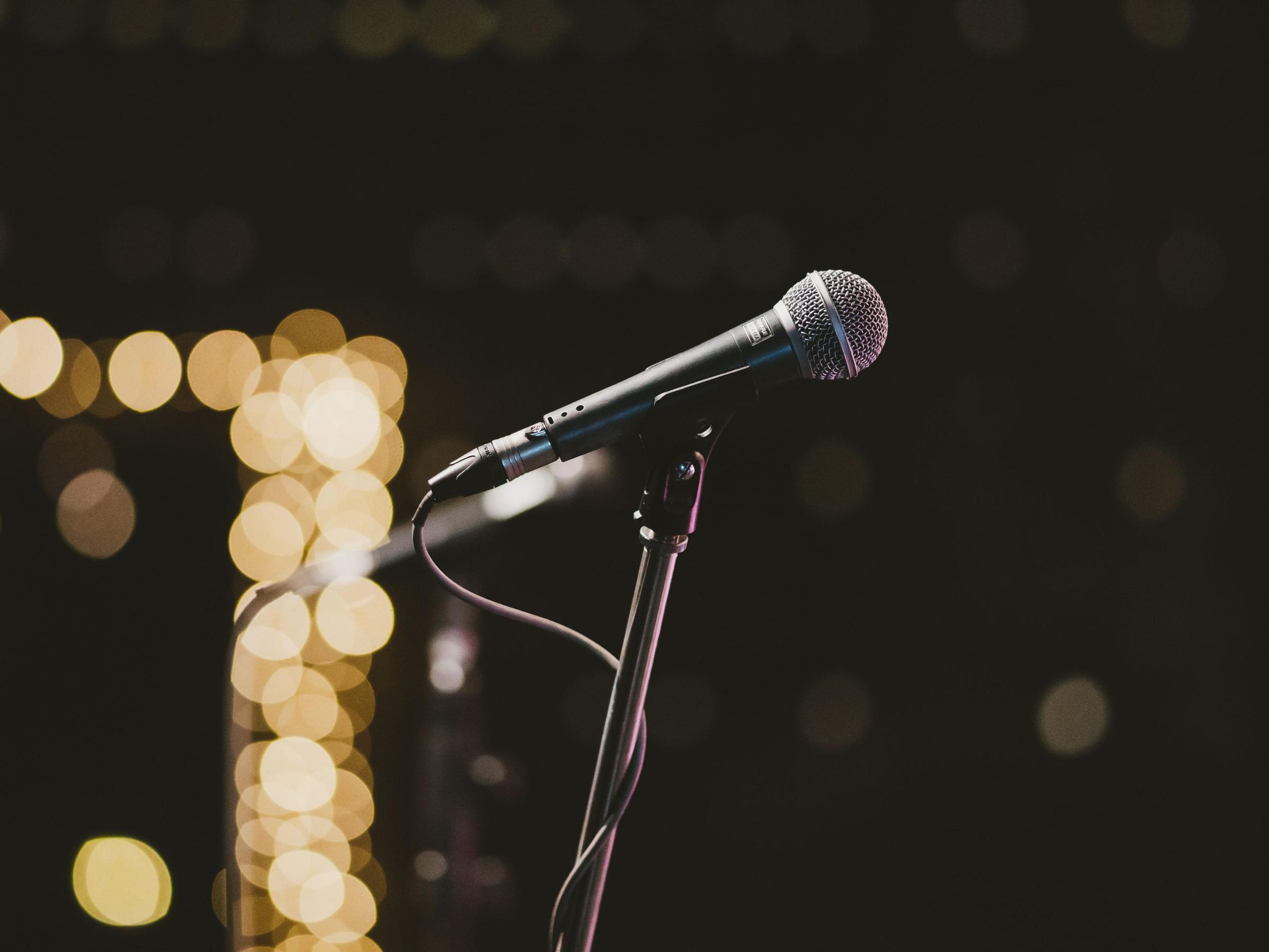 Illustrative photograph of a microphone on a stand in warm stage light