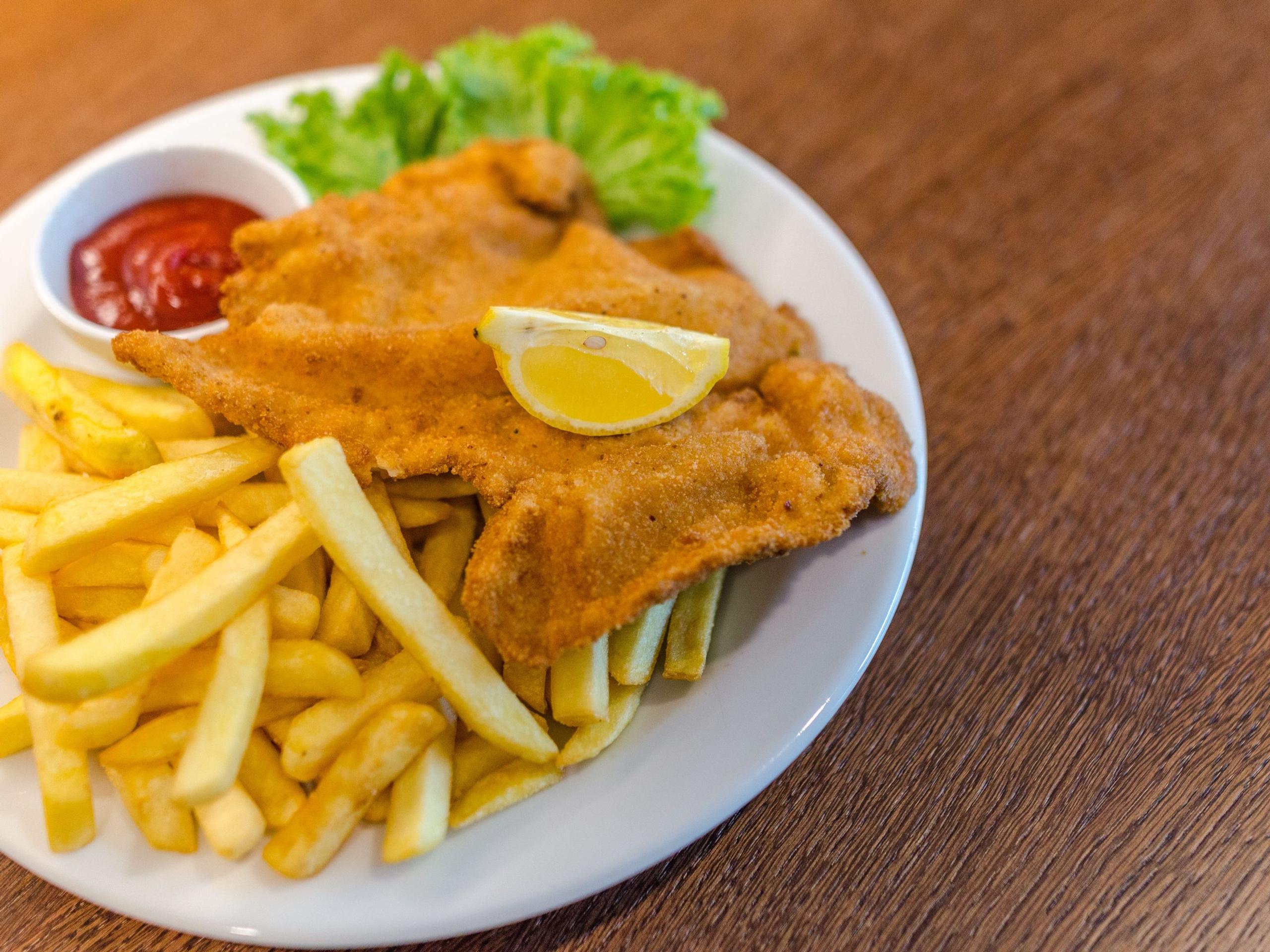 Illustrative photograph of a crumbed chicken schnitzel with chips and lemon; restaurant presentation differs