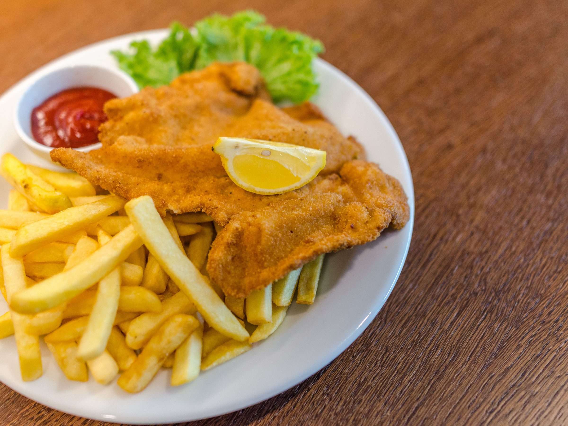 Illustrative photograph of a crumbed chicken schnitzel with chips and lemon; restaurant presentation differs