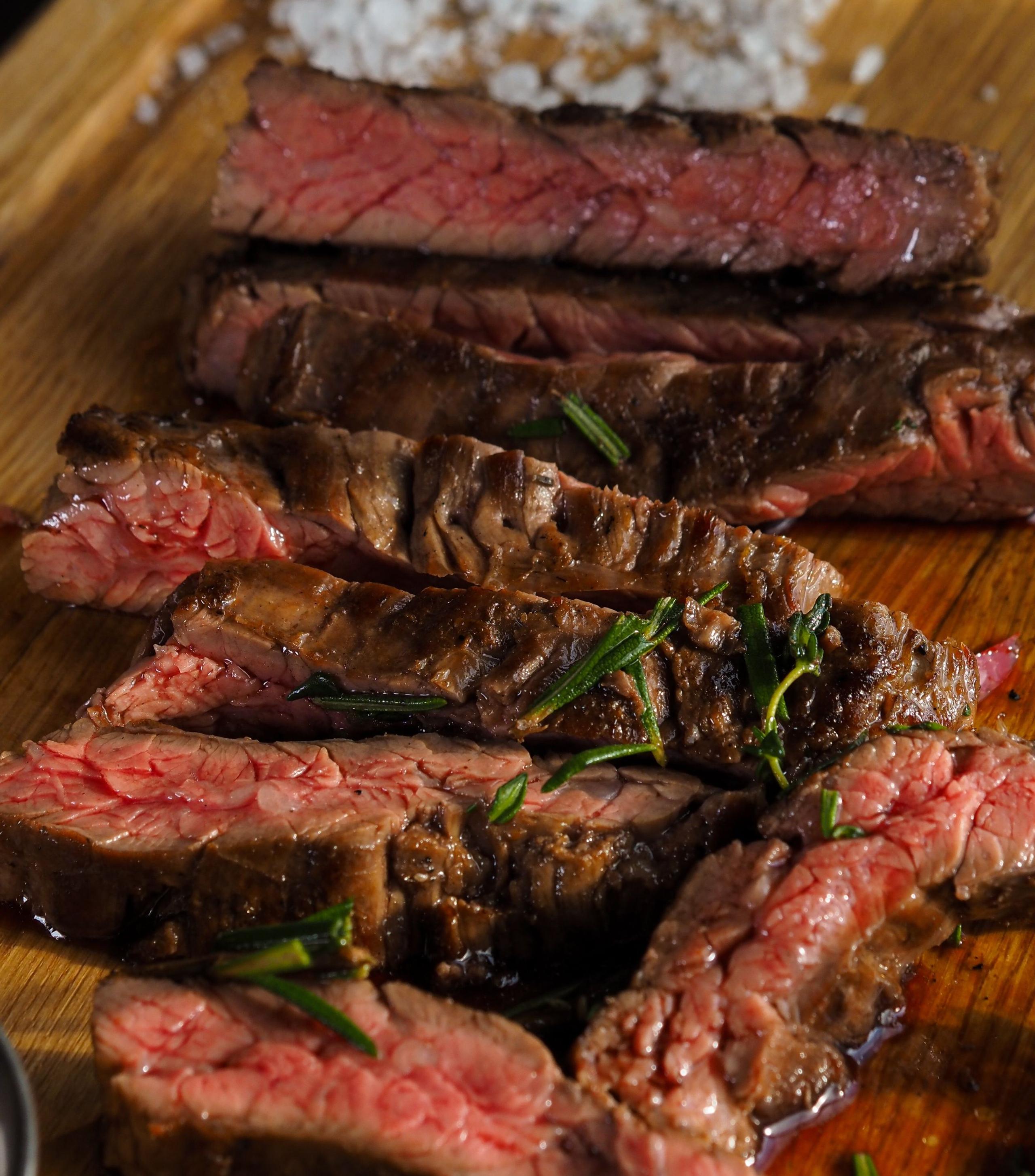 Illustrative stock photograph of a sliced rump steak, pink in the centre, on a wooden board with rosemary; restaurant presentation differs