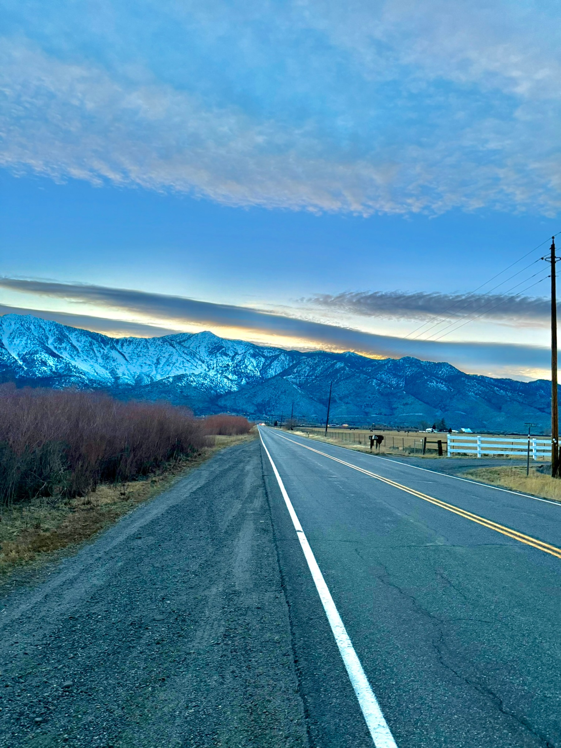 A road leading toward snow-covered mountains beneath a bright winter sky.