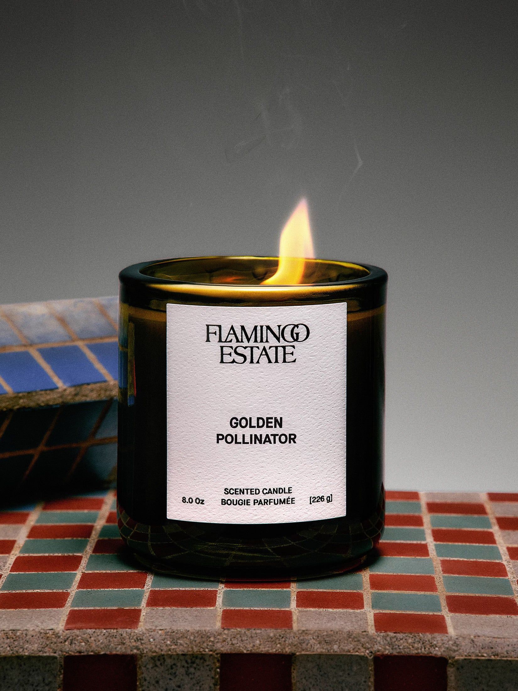 a product image featuring Flamingo Estate's Golden Pollinator soap and candle side by side in front of green packaging with a green bow. 