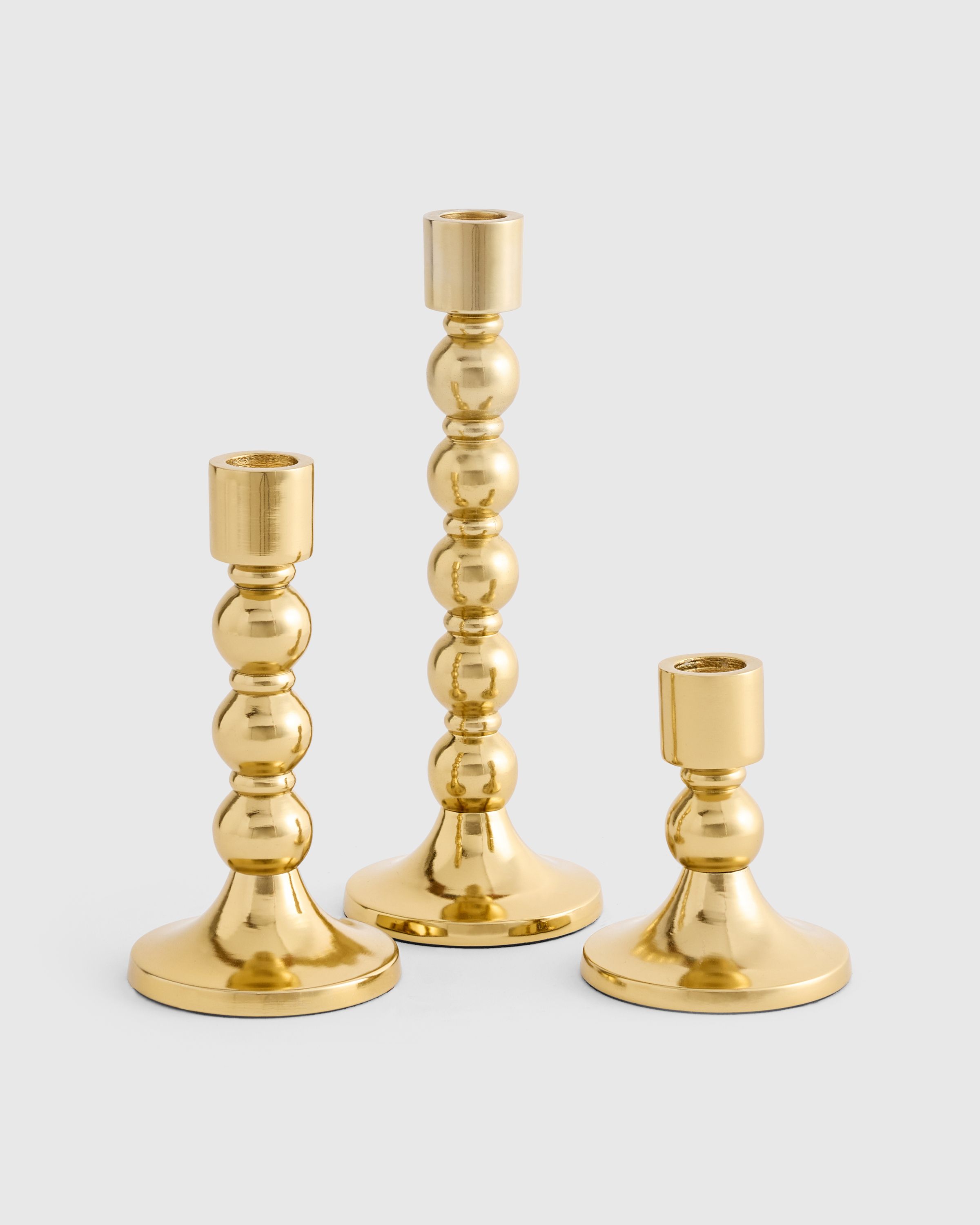 three brass candle holders of various heights. The base of the candlestick holders are in a classic bobble design. 