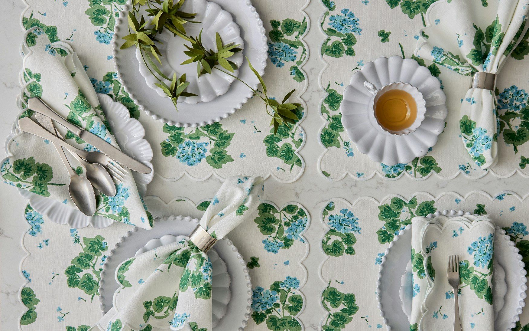 A table setting with four placemats in a blue and green geranium print. 