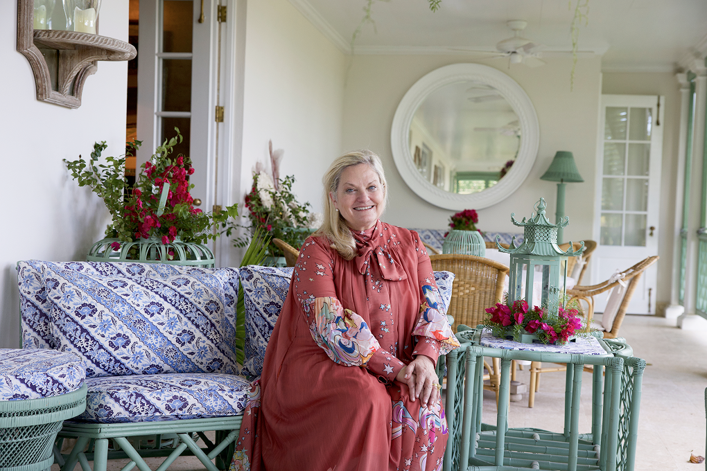 Designer Amanda Lindroth sits on a blue and white patterned rattan couch that has been pained green. 