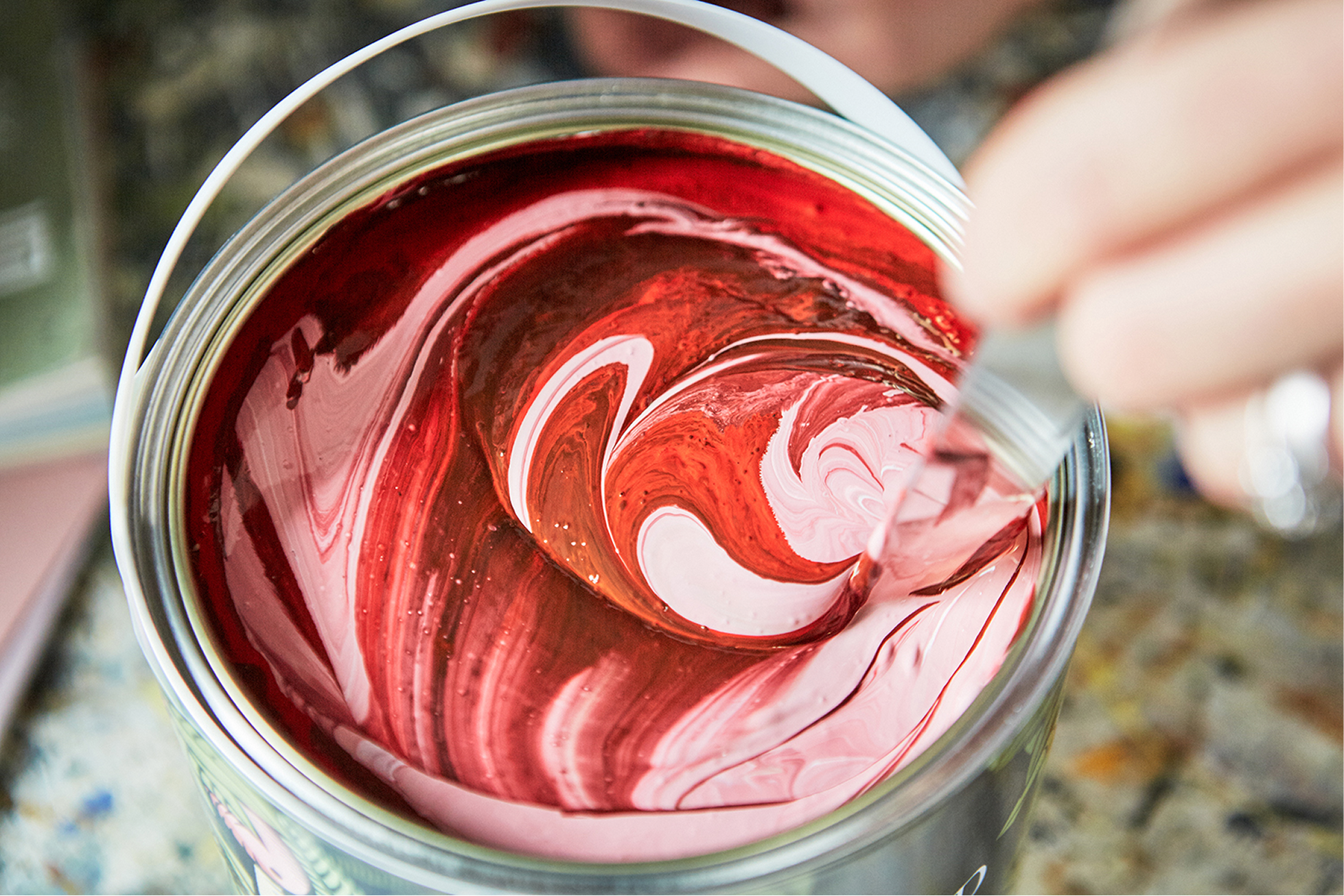 an open can of Edward Bulmer wall paint. The paint has a base of light pink with swirls of rich red being mixed in by hand.