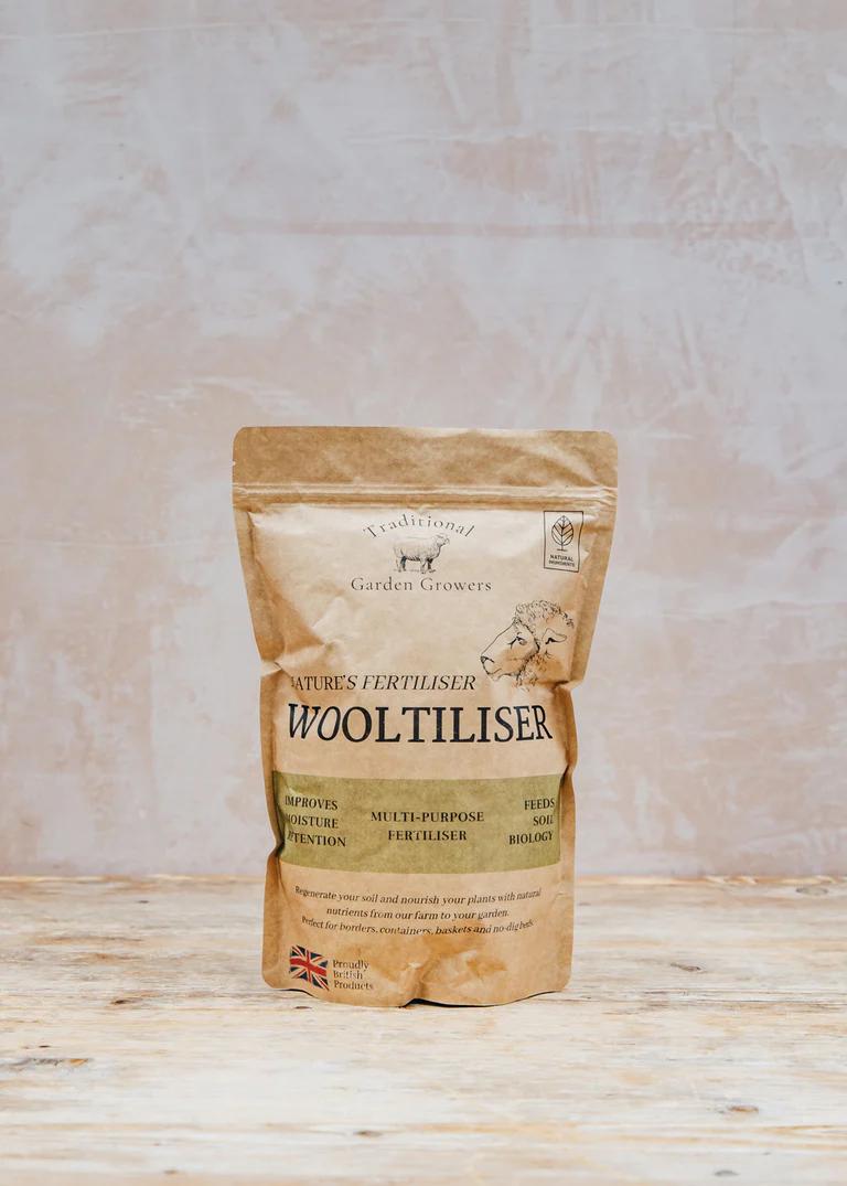 A product image of a bag of Wooltiliser. The bag is small and brown, with the logo and a sheep on the front.