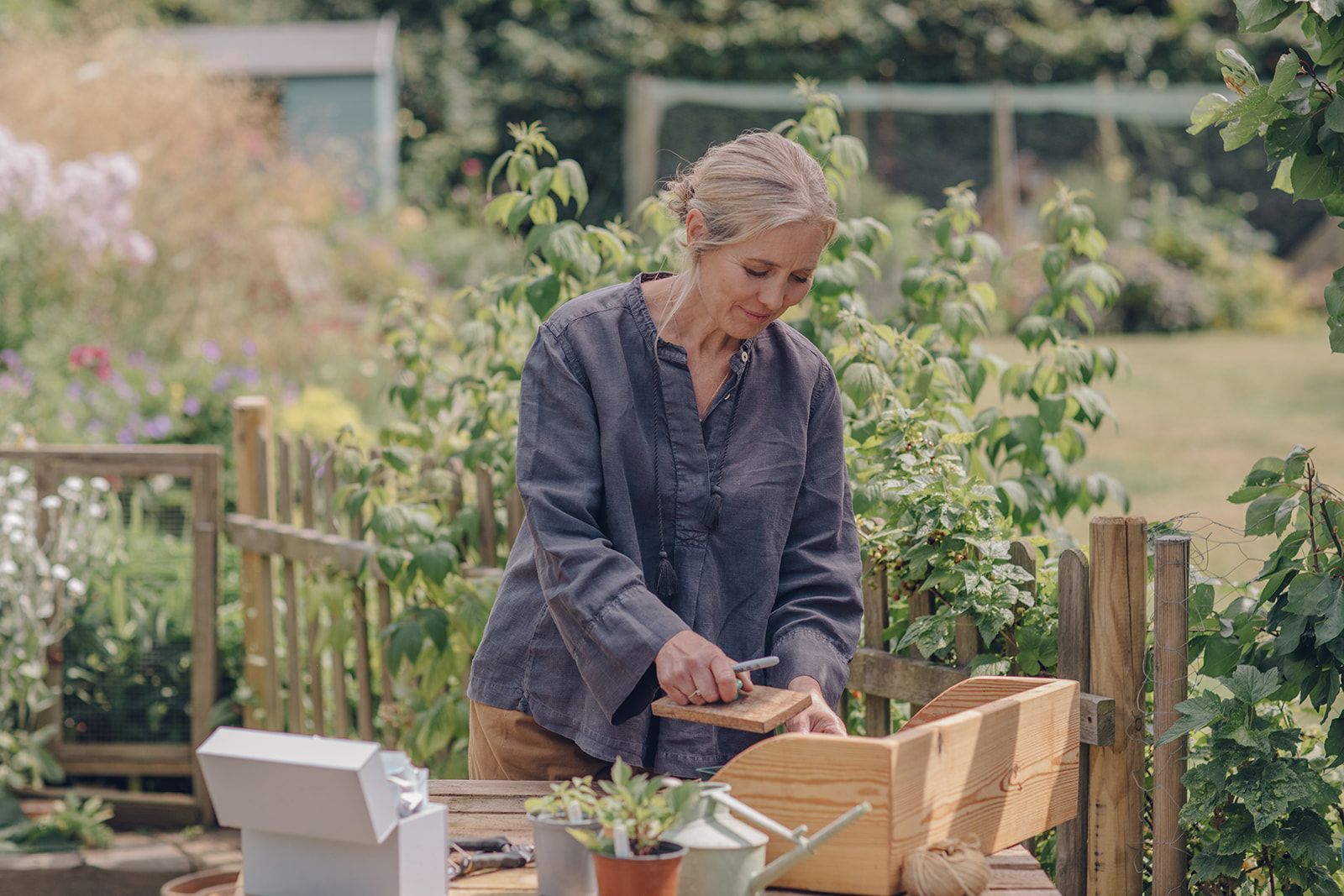 Clare Foster stands over her potting table. She is using a wooden seed tamper to press her newly planted seeds into the soil. 