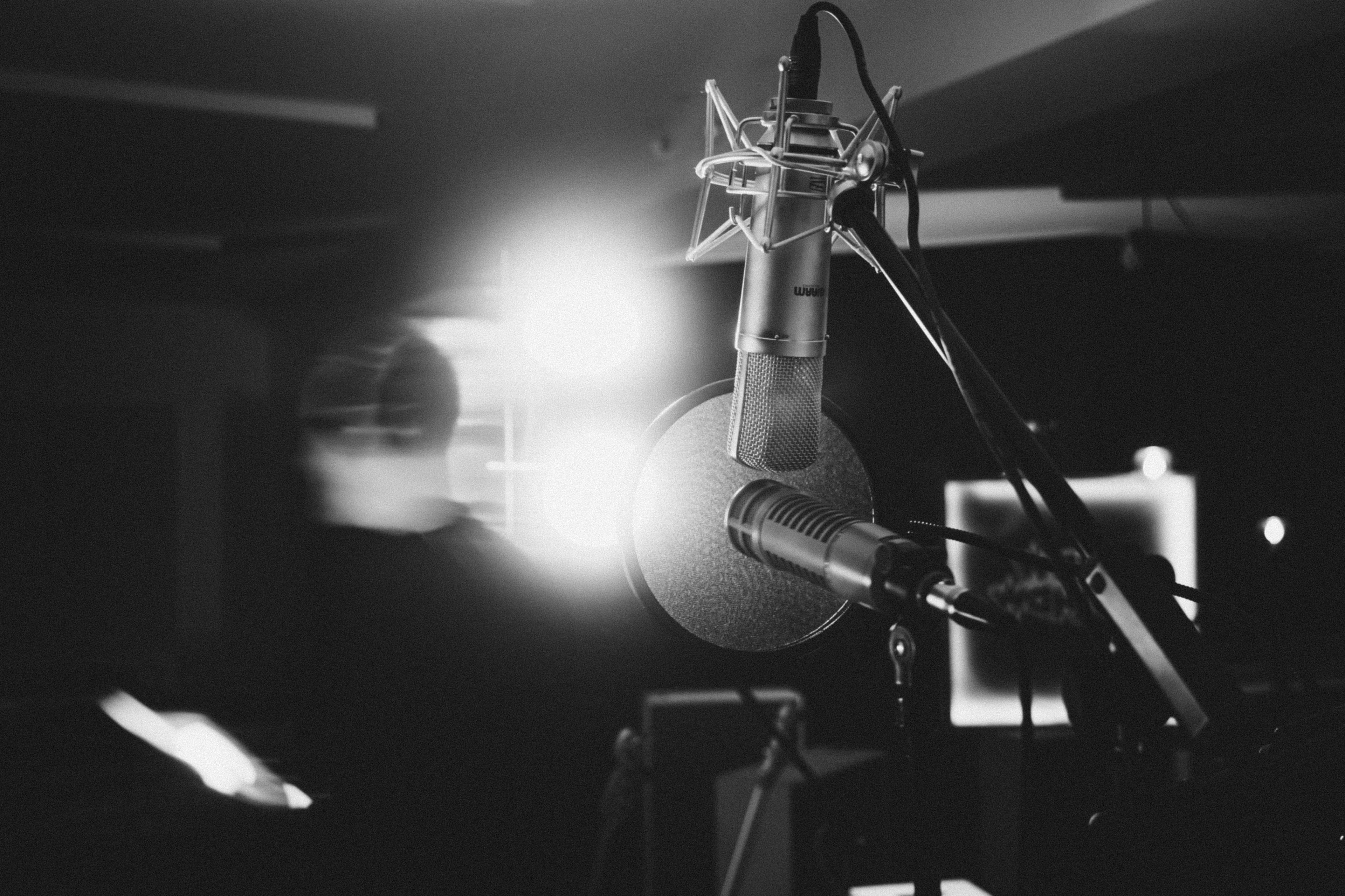 A picture in black and white from inside the studio: two mics are shown and in the background a vague silhouette of the rapper moving