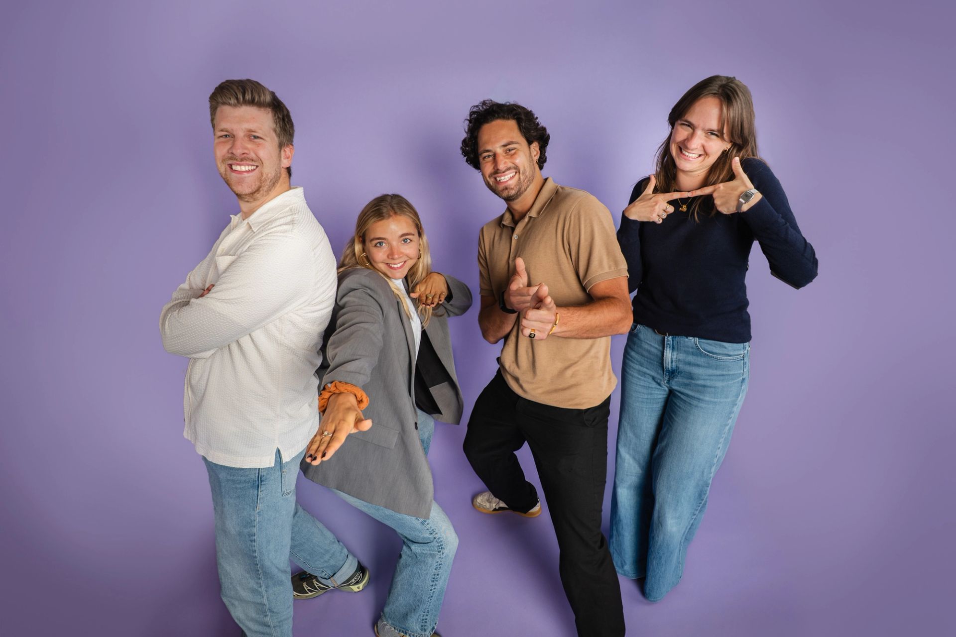Vier collega's poseren speels tegen een paarse achtergrond bij een teamportret in de studio.