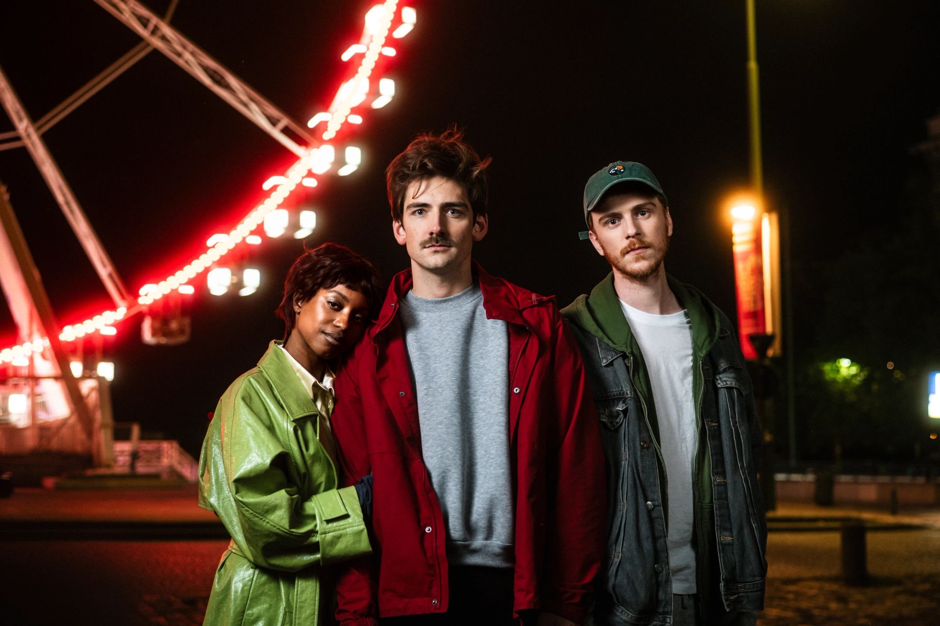 Trois personnes se tiennent ensemble la nuit près d'une grande roue lumineuse.