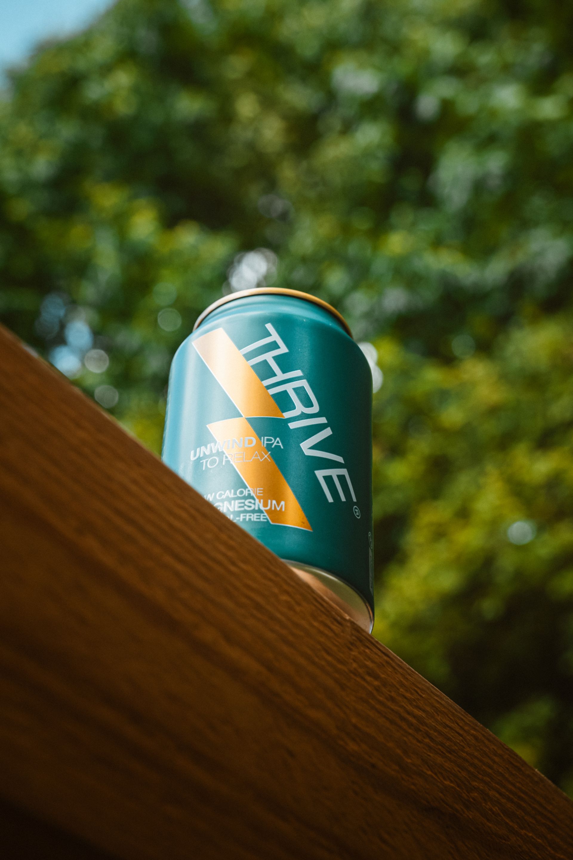 Een turquoise Thrive-blikje op een houten rand tegen wazig groen gebladerte.
