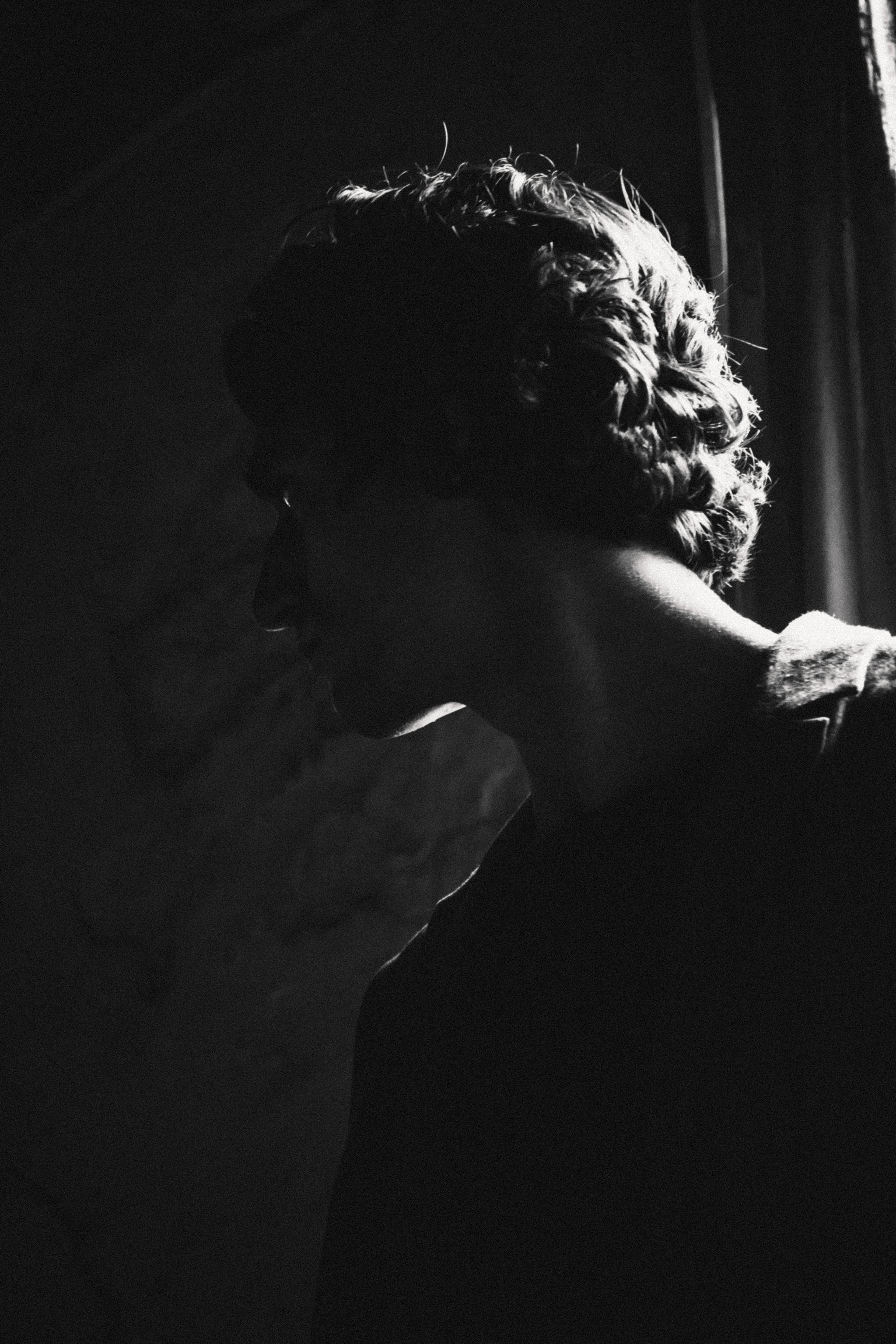 Tamino in a dark room with a faint light showing part of his face.