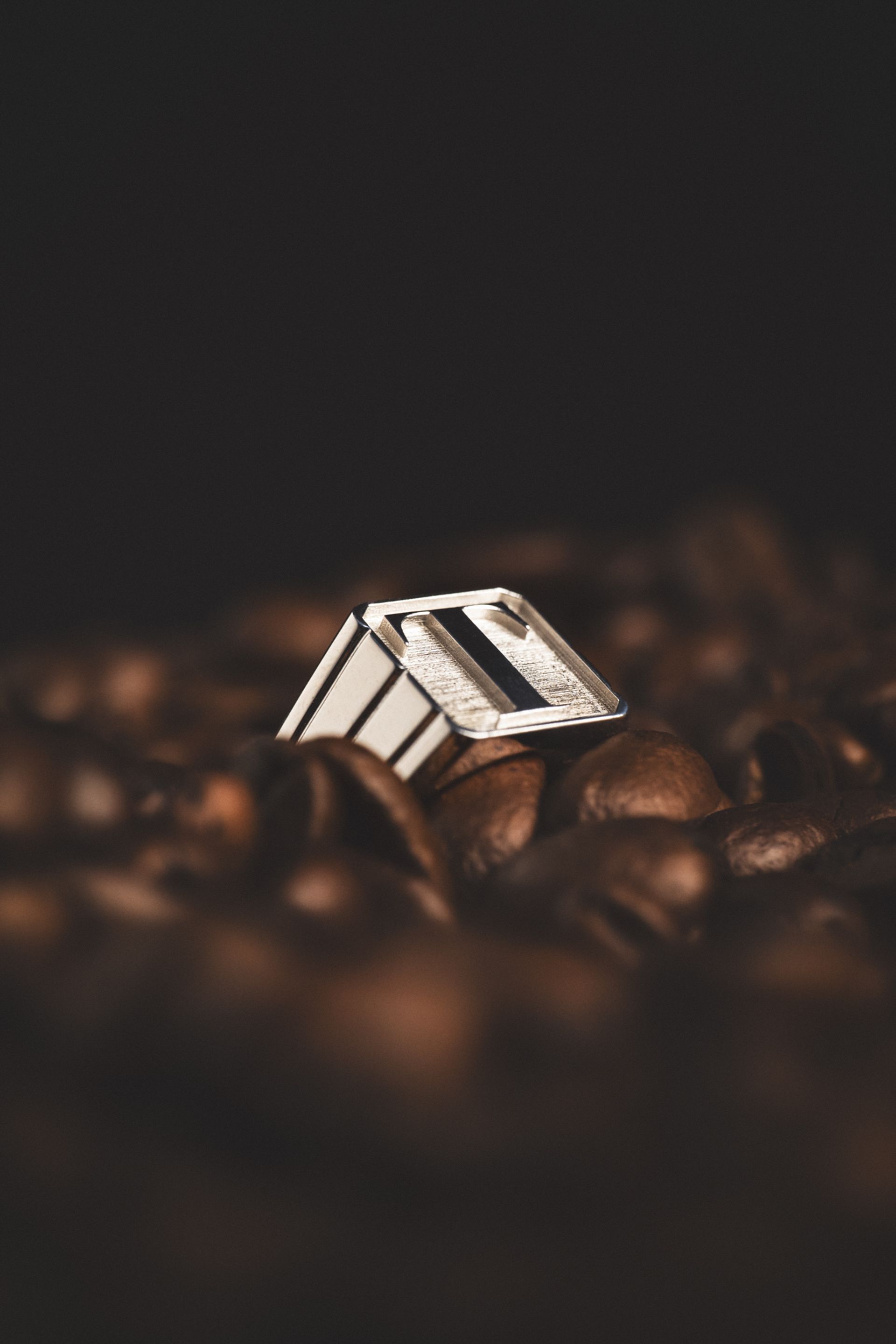 A silver ring showcased on a bed of coffee beans with a dark background.
