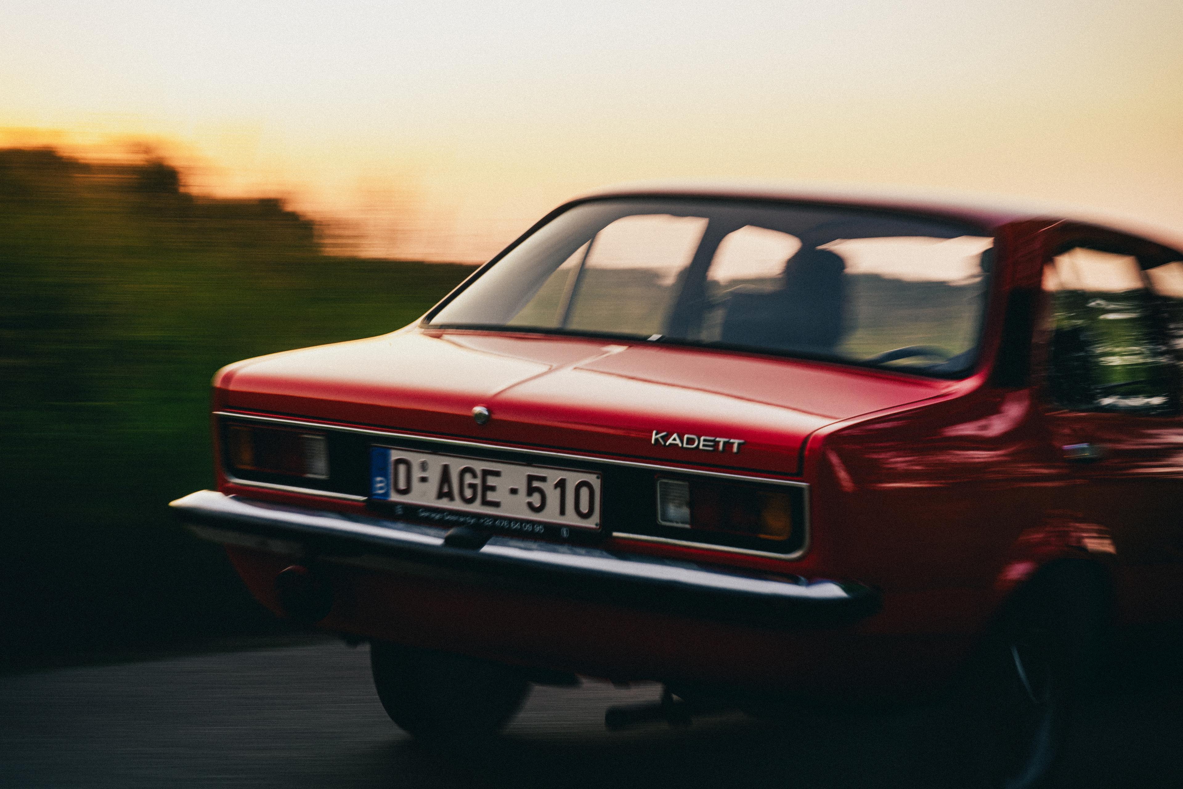 A red bright old-timer car driving by in the warm sunlight of the setting sun