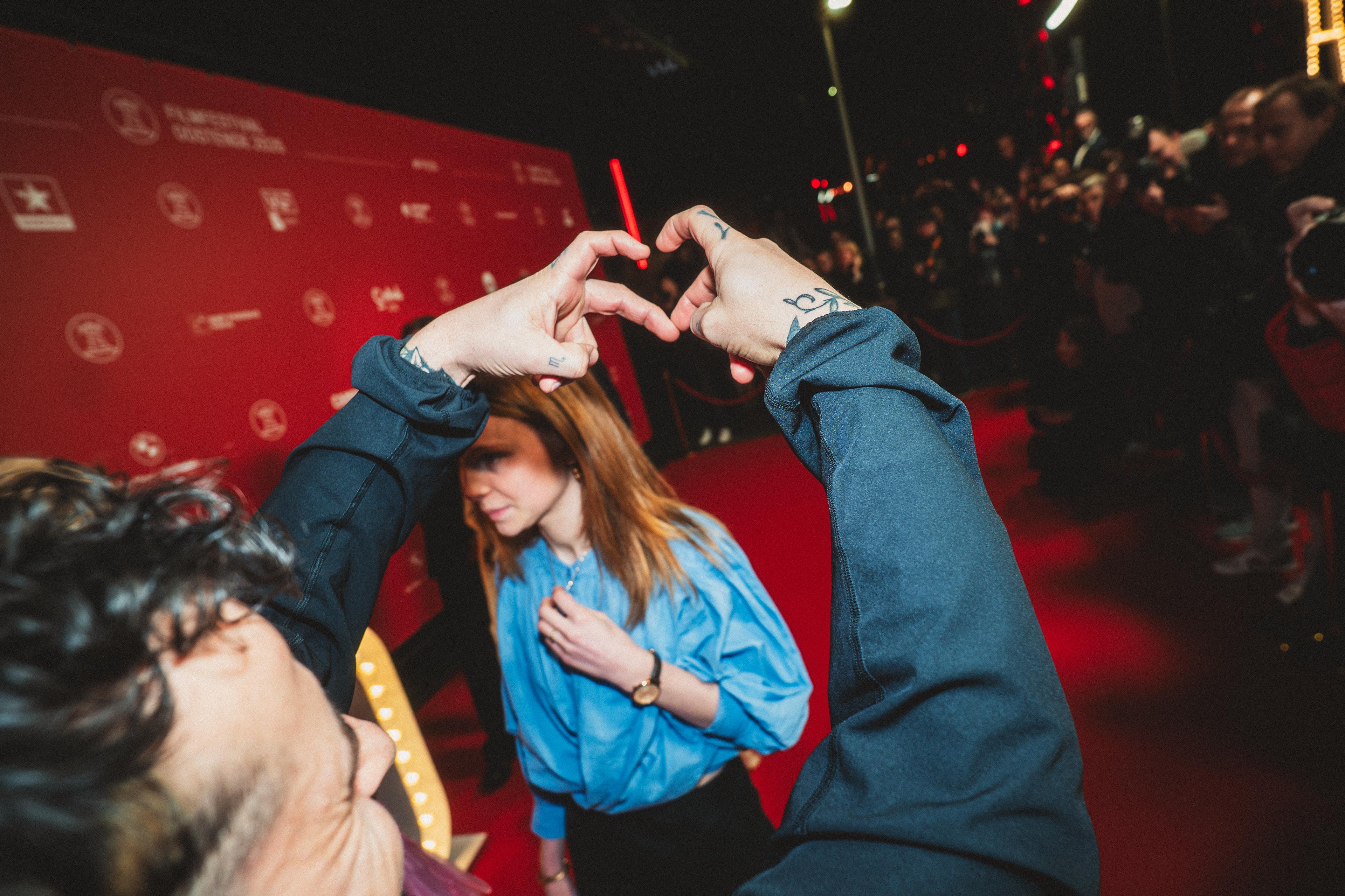 Zwangere Guy making a hearth symbol with his hands. Iin the background you see the bright red color of the red carpet of film festival oostende.