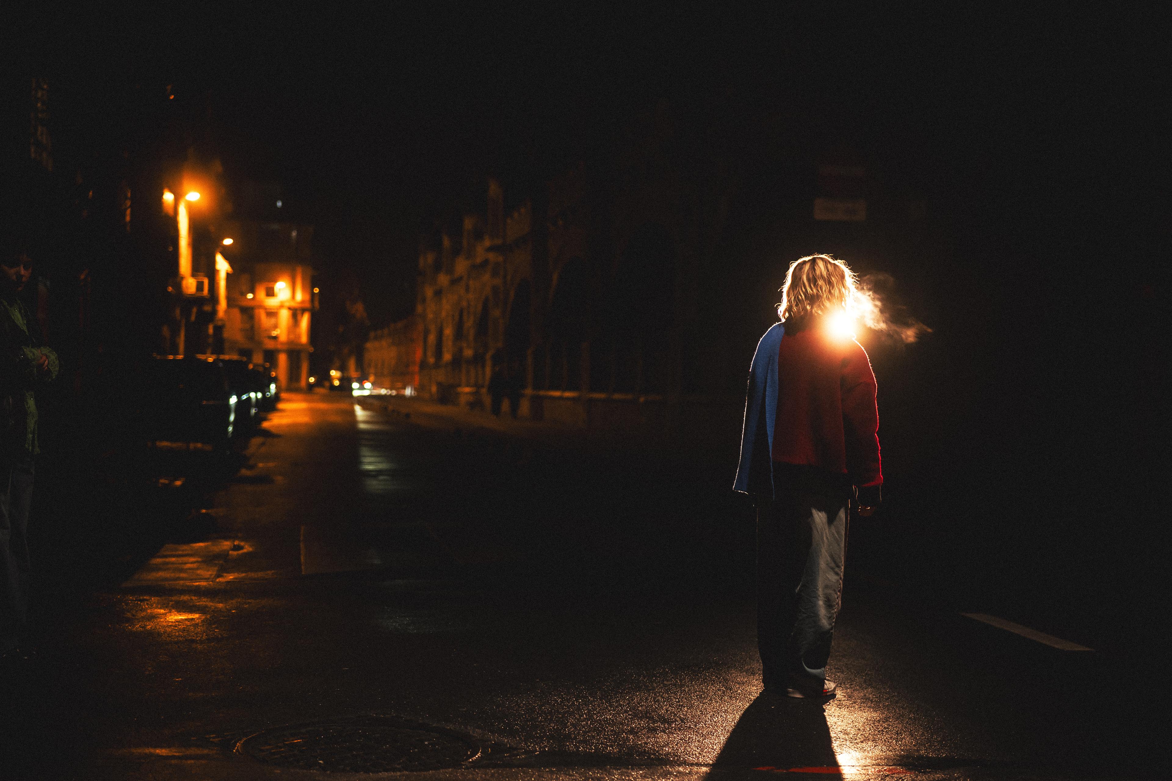 Silhouette of a girl illuminated by a street lantern, exhaling a visible puff of warm breath in the cold night air.