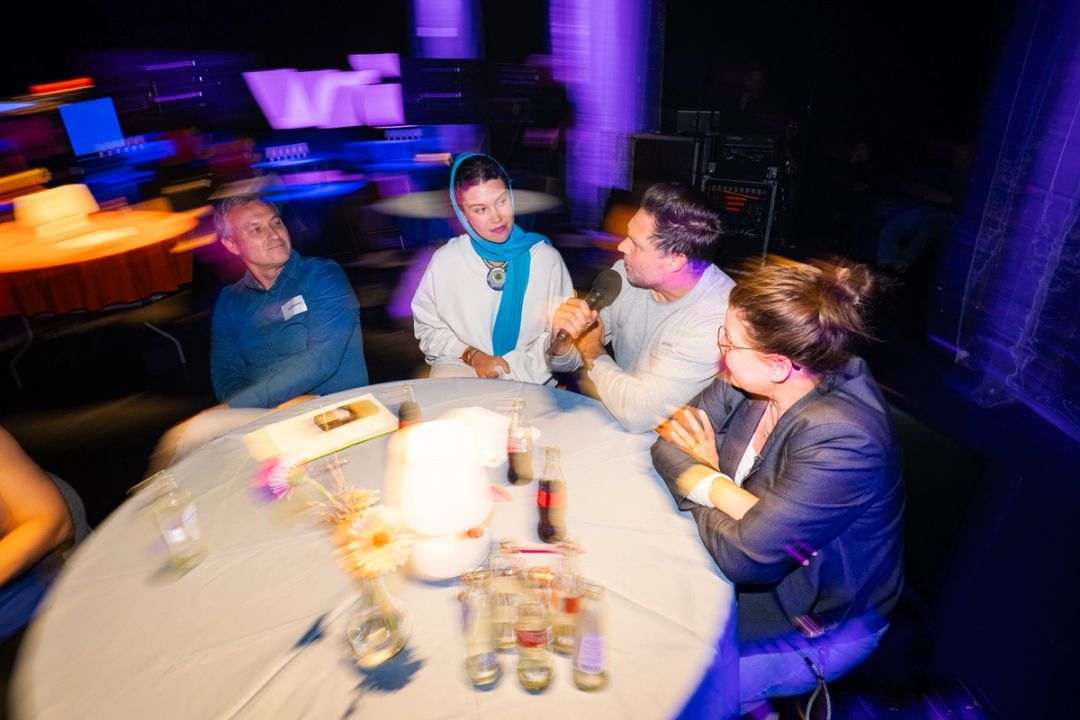 Table ronde grand angle: un homme en chemise bleue, une femme au foulard bleu, un homme parlant au micro et une femme en blazer.