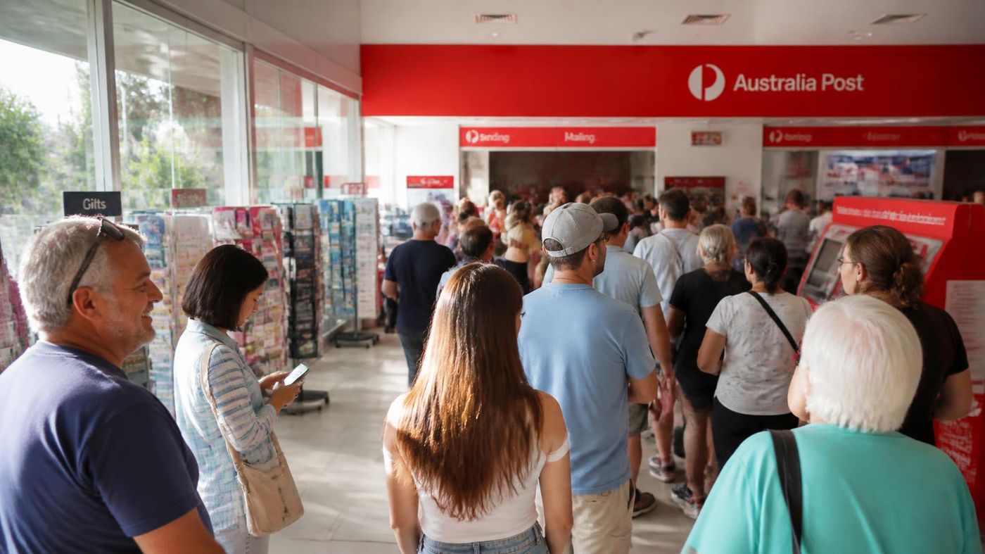 Long queue of people inside an Australia Post branch waiting near the Sending and Mailing counters.